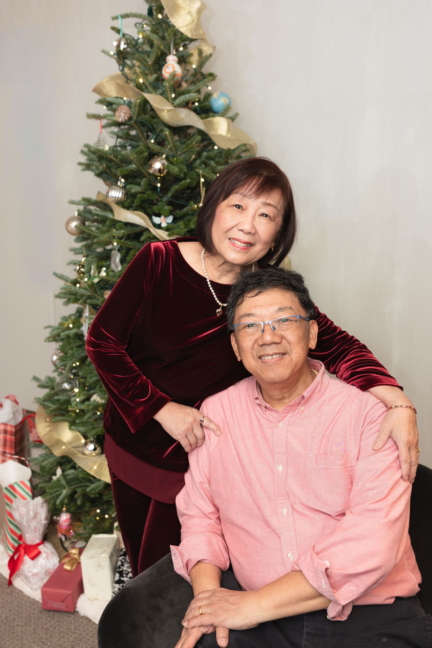 A festive holiday portrait in front of a decorated Christmas tree with wrapped presents underneath.