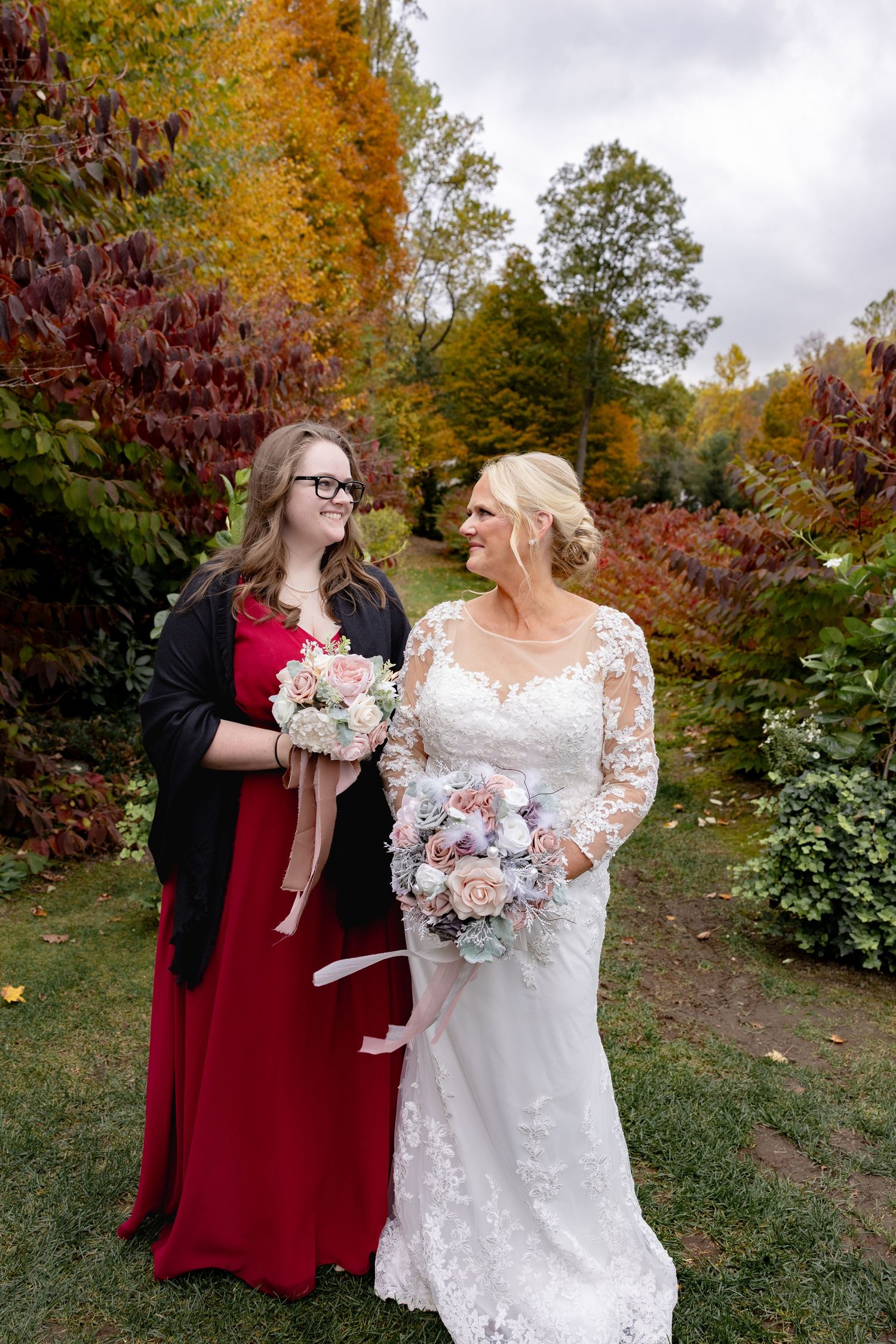 Wedding party celebrates in a garden with fall colors as backdrop while holding delicate pink and white bouquets.