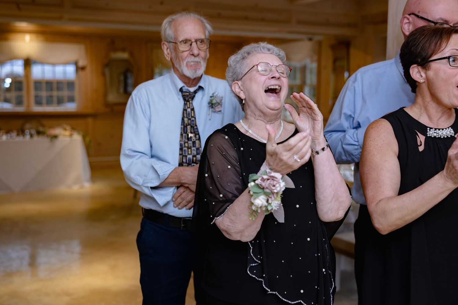 A group of people laughing together in a warm wooden-paneled room during a social gathering.