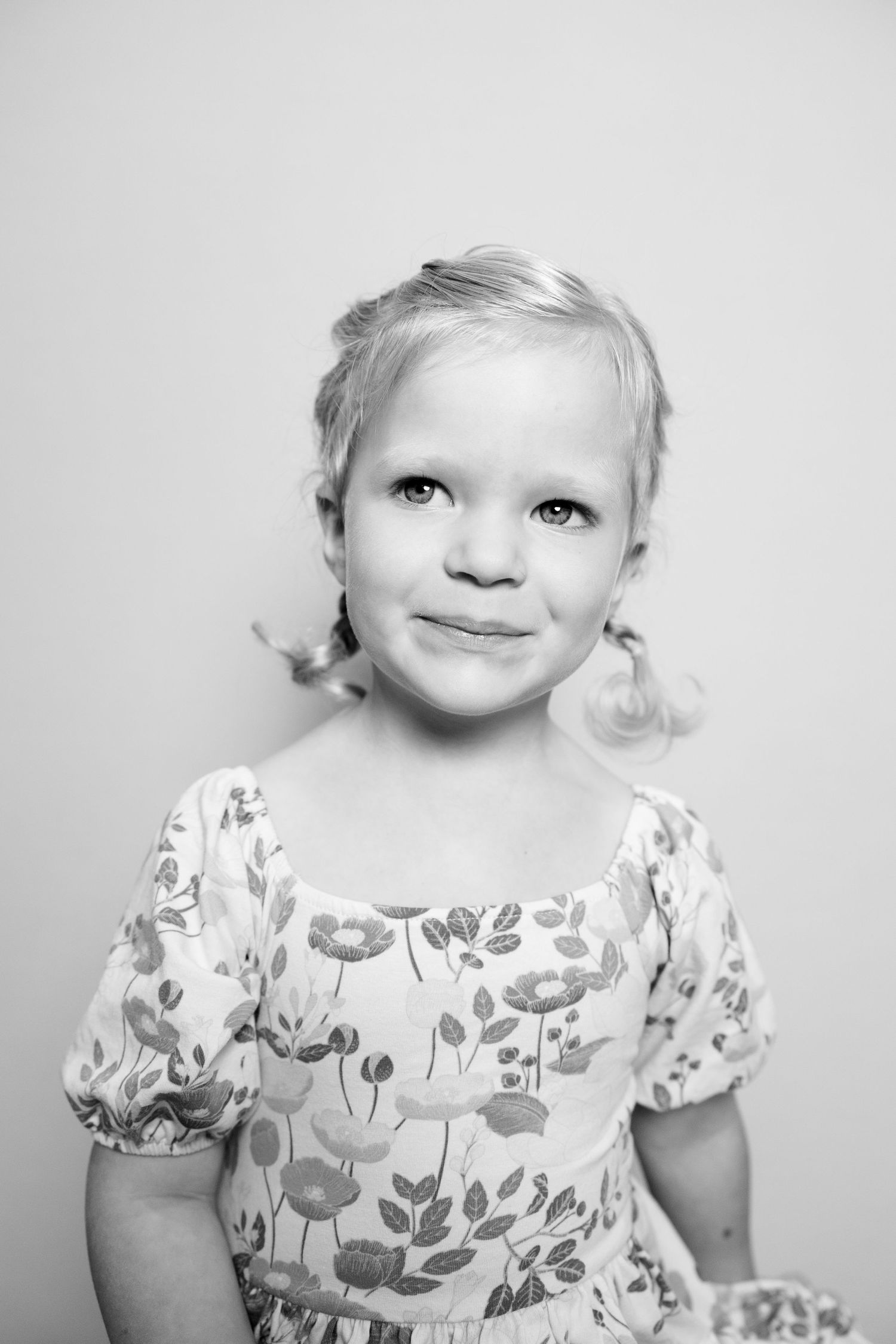 A series of black and white portraits showing a young child wearing a floral print dress with short puff sleeves.