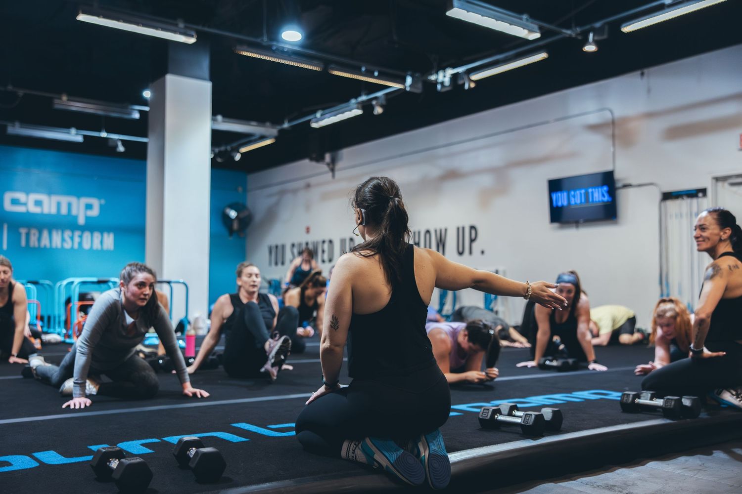 Group fitness class performing synchronized floor exercises in a modern blue-themed gym space.