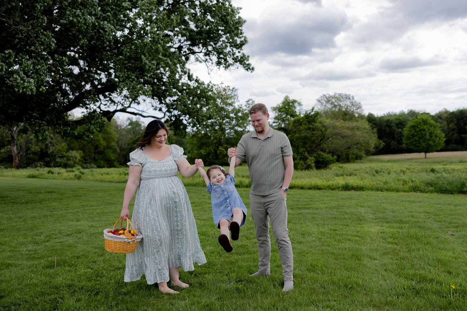 A family enjoying a spring day together on grassy meadow holding hands with a picnic basket.