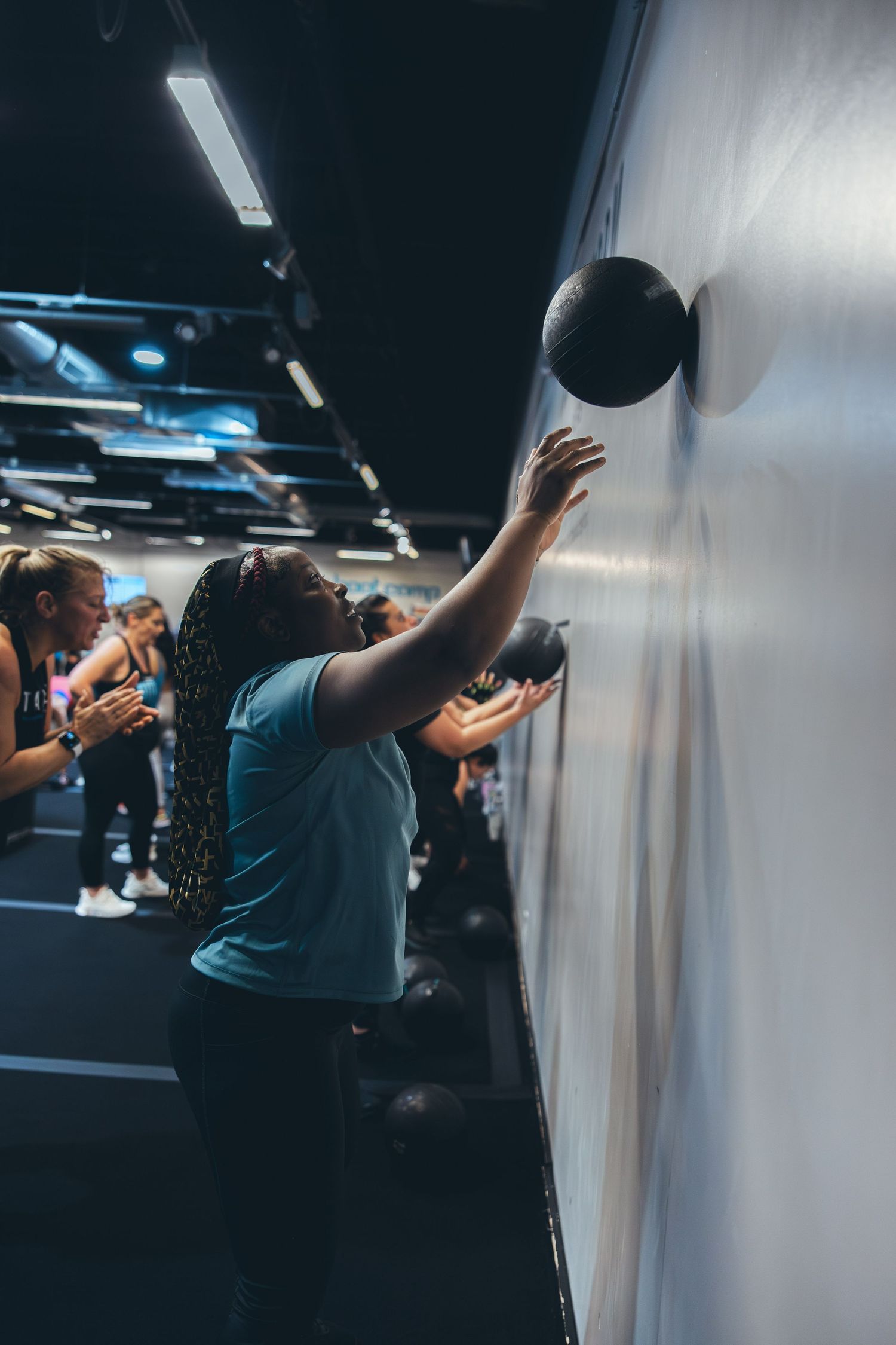 Athletes perform wall ball exercises with medicine balls during an intense fitness class at indoor gym.