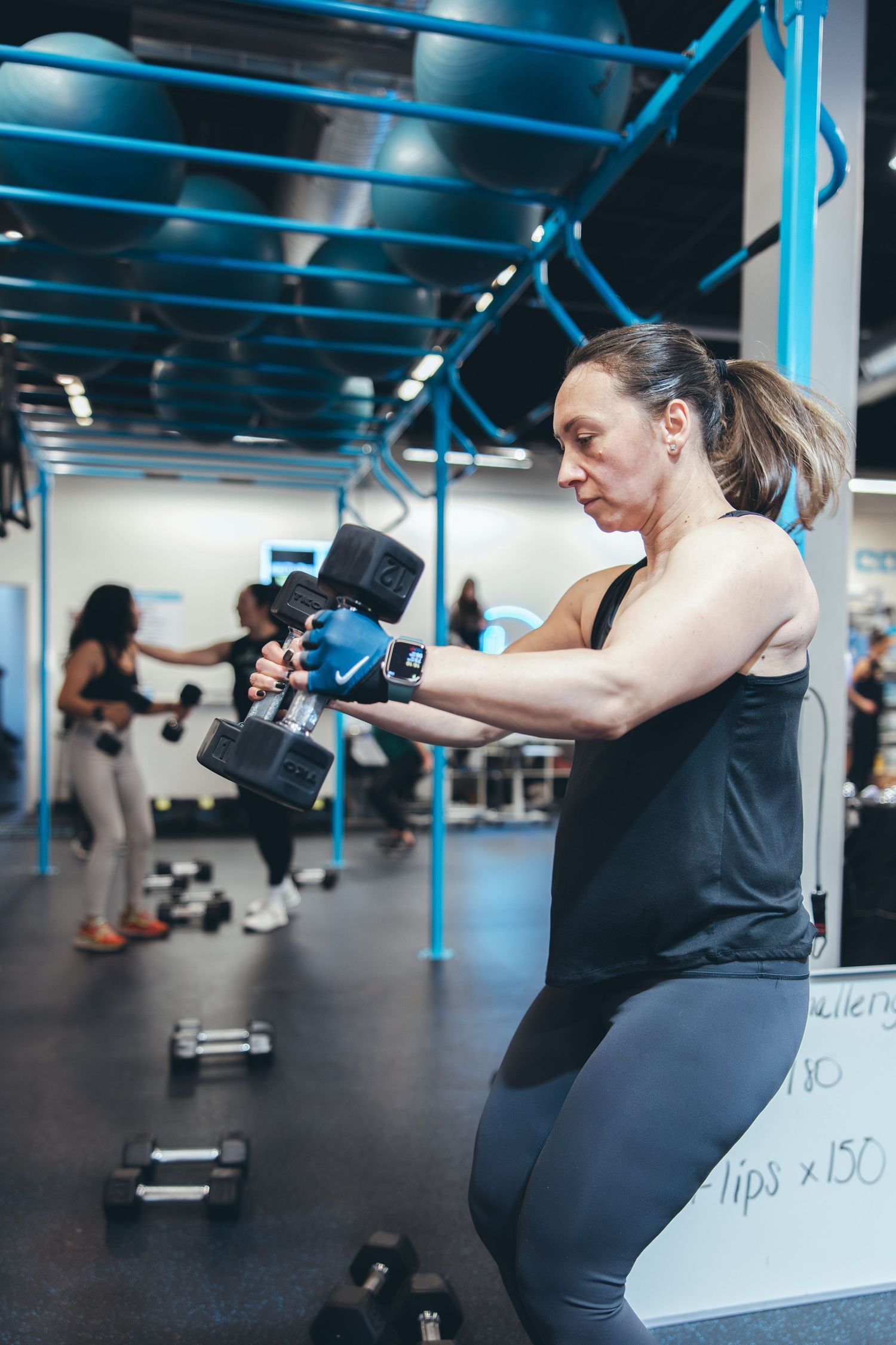Focused exerciser performing dumbbell workout in modern gym with blue structural elements.