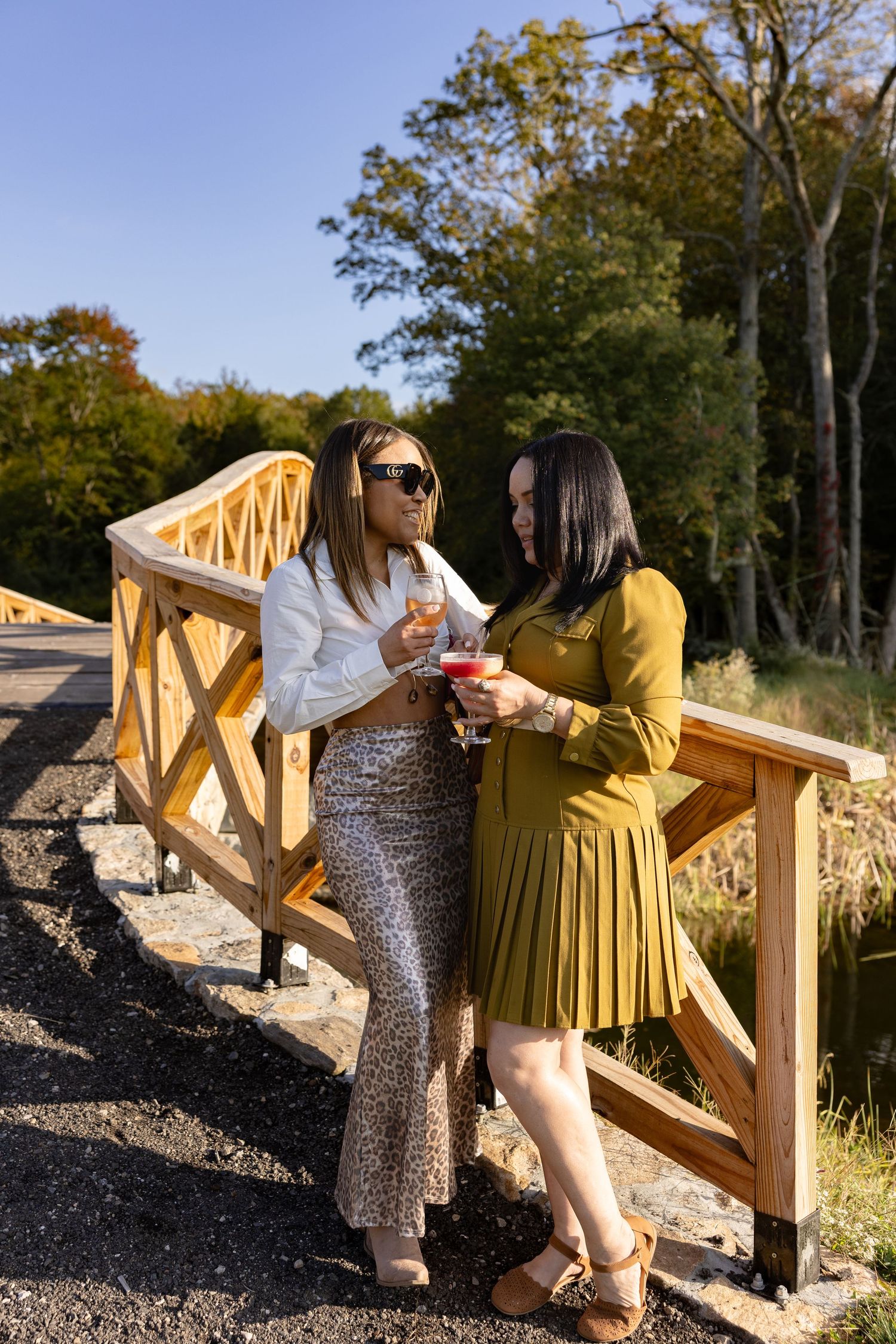 Two people enjoying drinks while standing on a wooden deck surrounded by autumn trees.