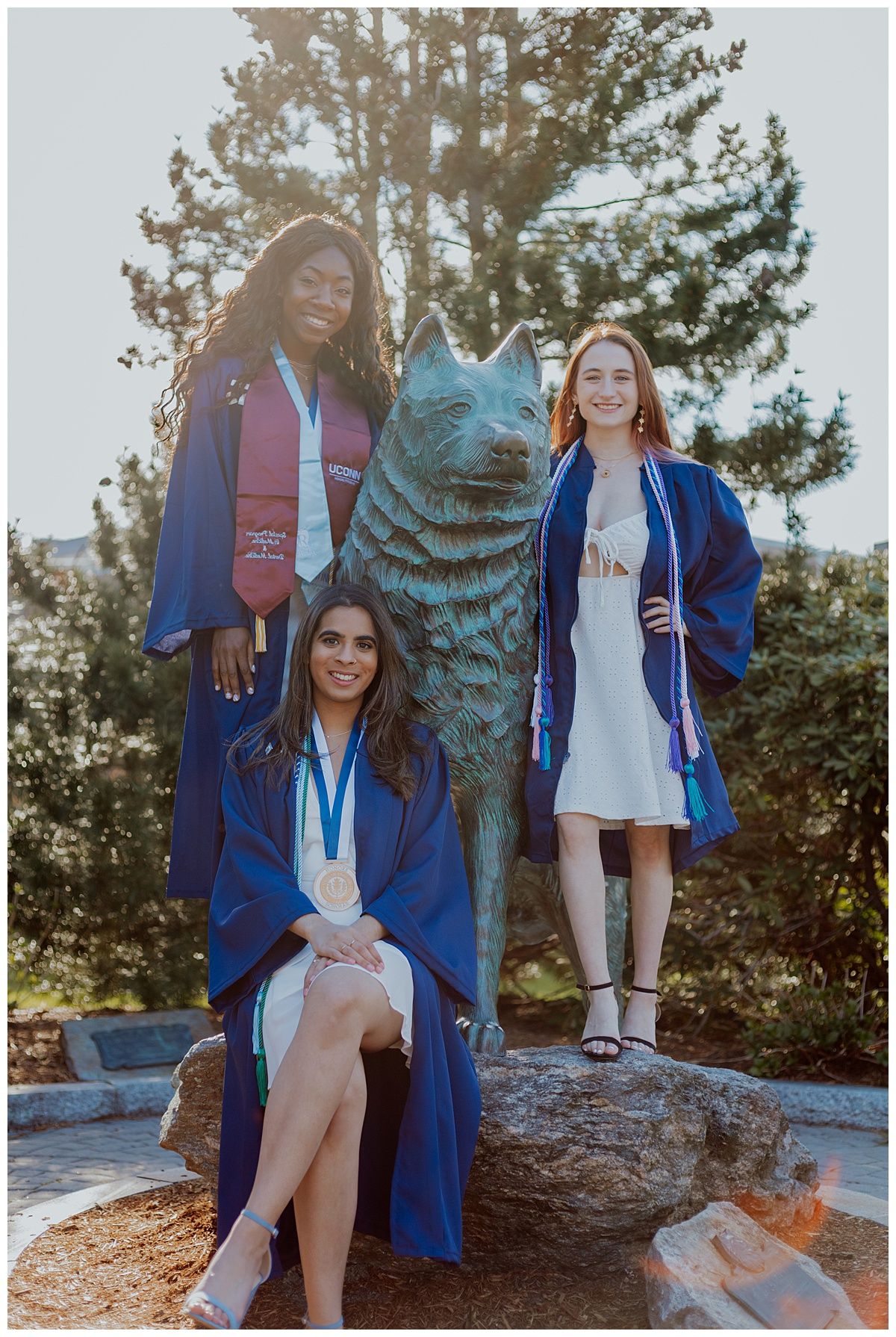 Three graduates pose with the UConn Husky mascot statue during commencement celebrations.