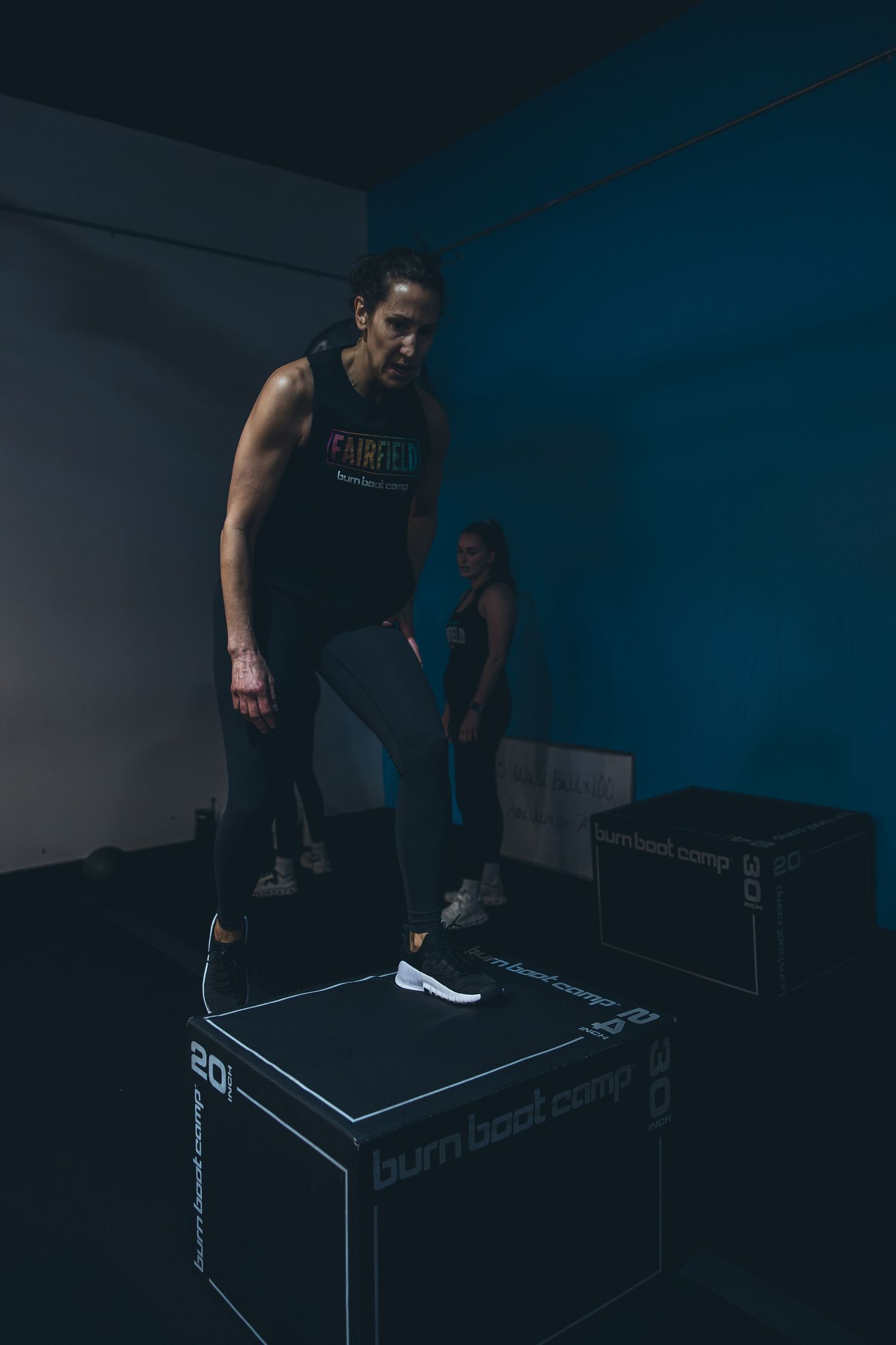 Athlete performing box step exercises in dimly lit fitness studio with blue lighting.
