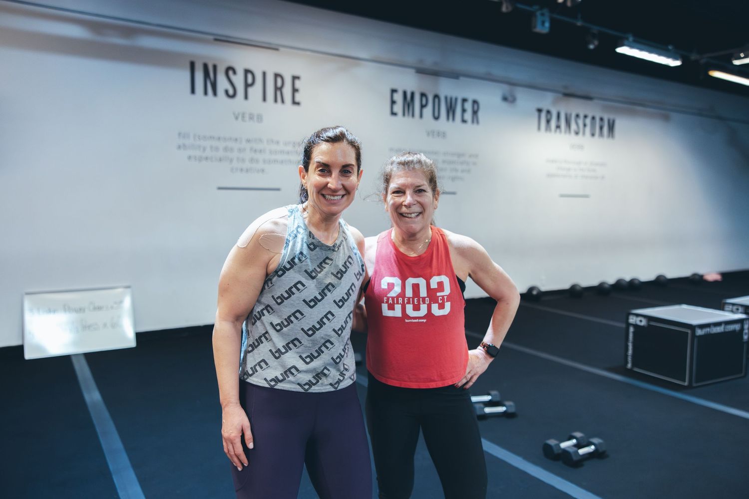 Two athletes standing together in workout clothes in front of an inspiring gym wall display.