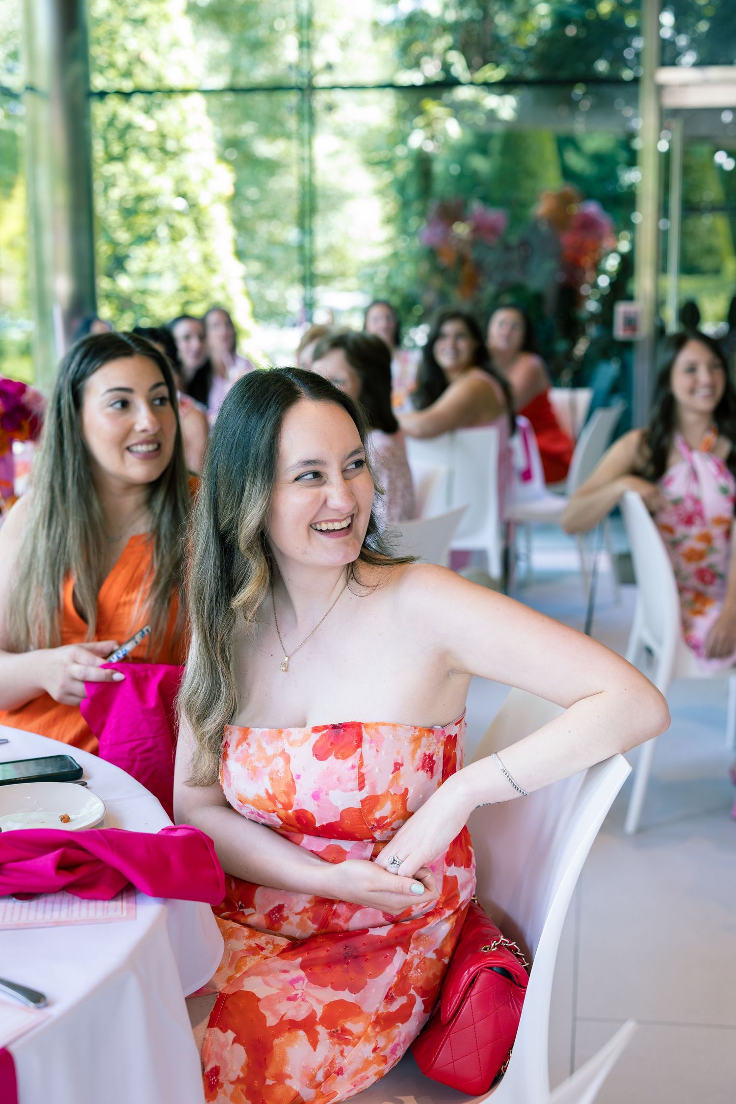 Guests in colorful dresses enjoying a lively celebration at an outdoor covered venue with white chairs.