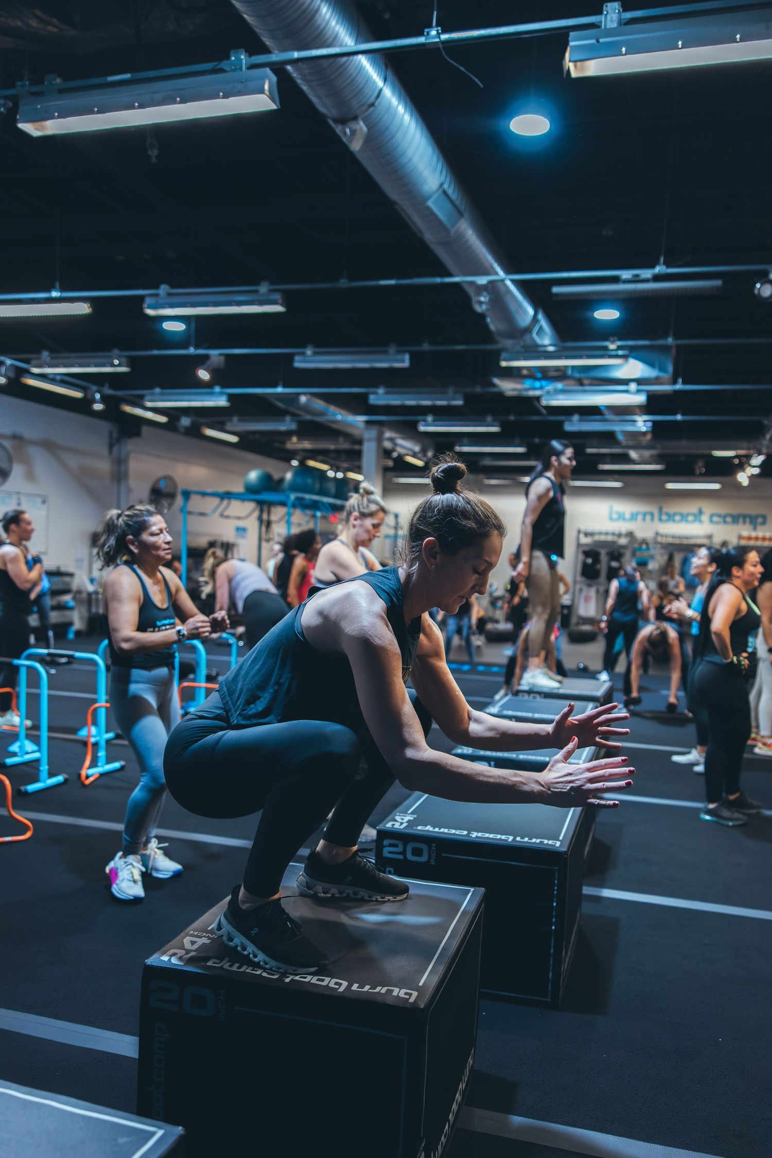 Group fitness class participants doing box step exercises in modern gym facility.