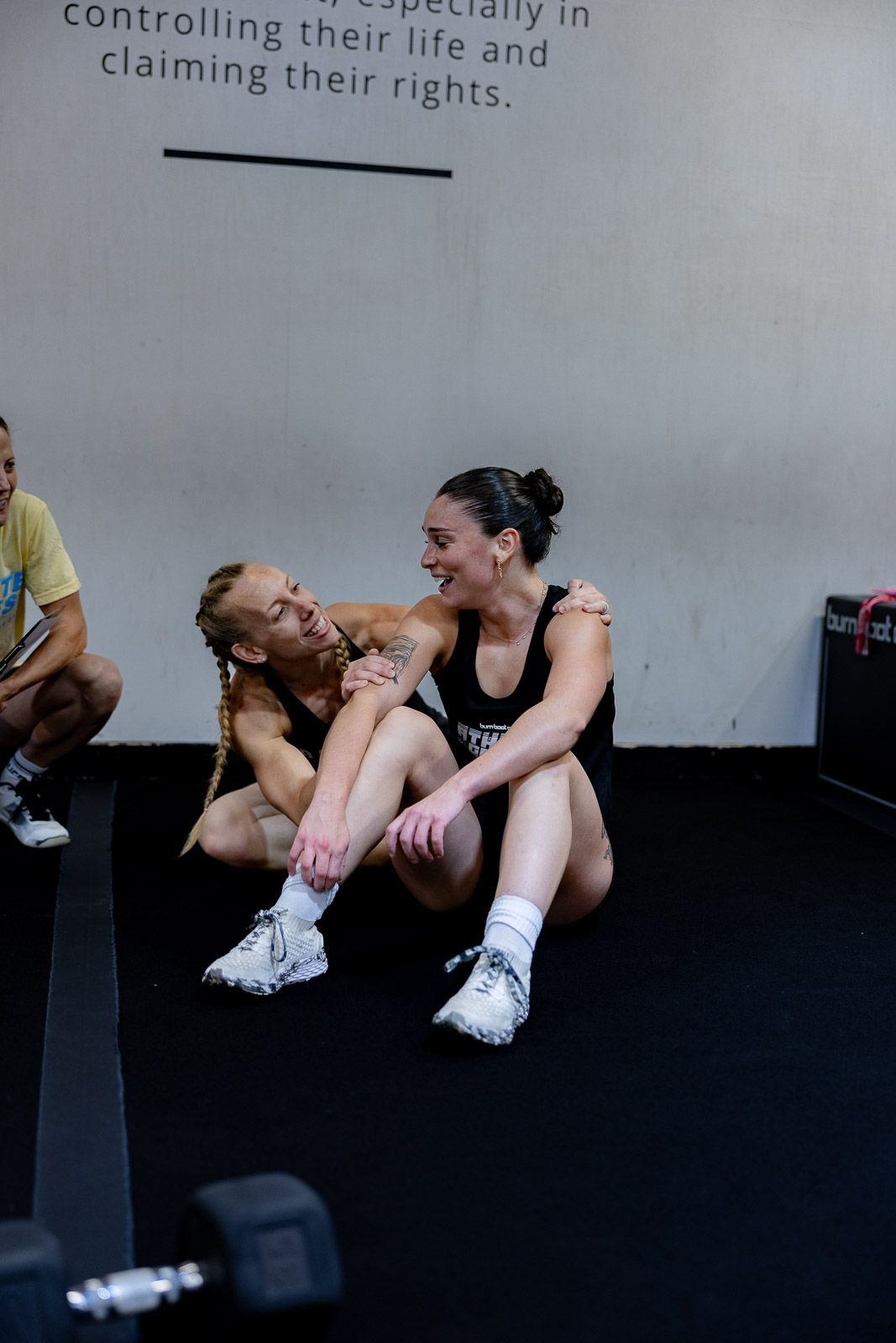 Athletes share a joyful moment while resting on the floor during a workout session at the gym.