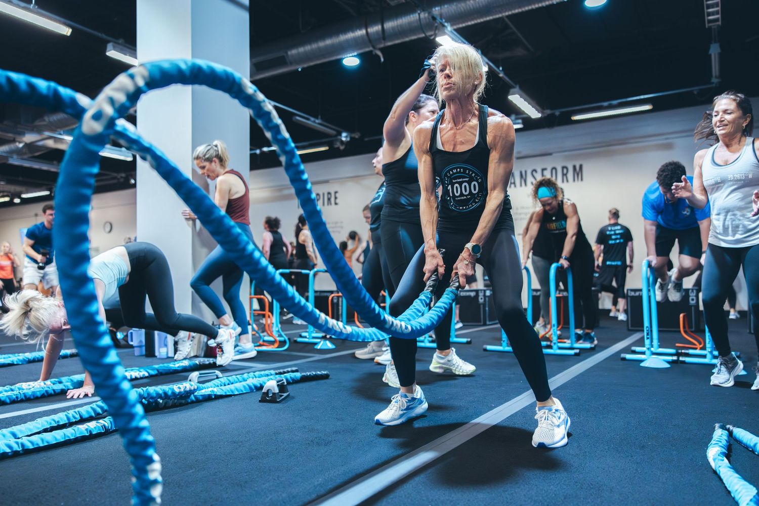 Fitness enthusiasts working out with blue battle ropes during a high-intensity training session in a modern gym.