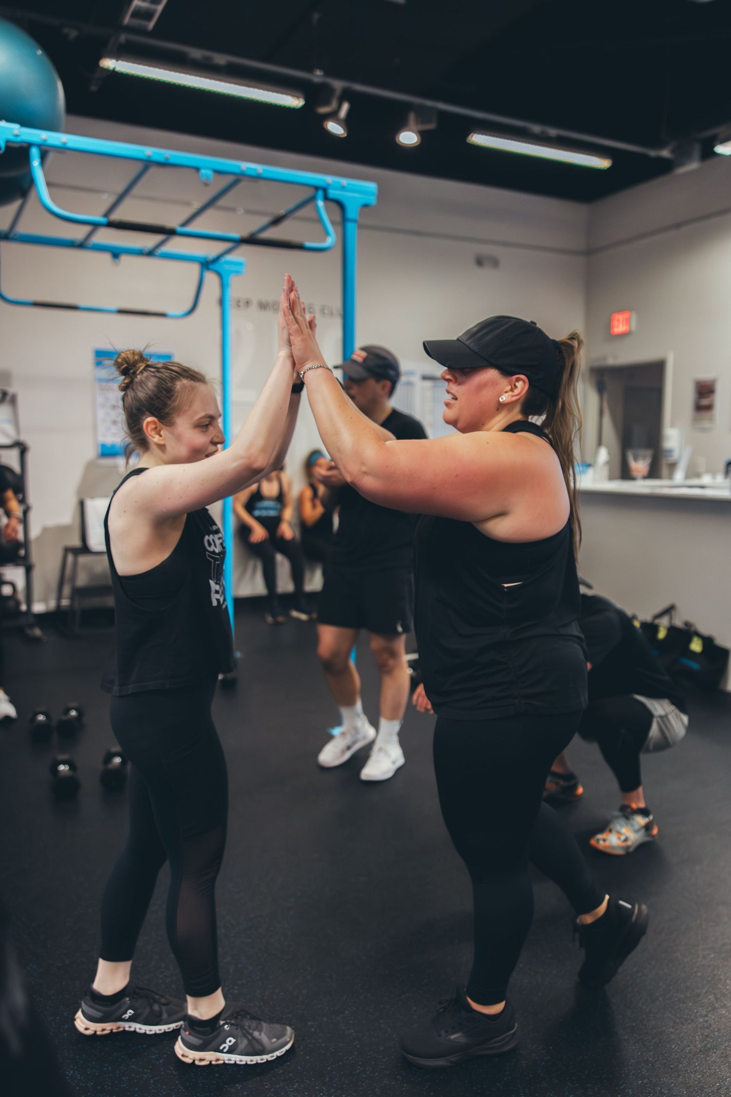 Two people in athletic wear giving each other a high-five during a group workout session.