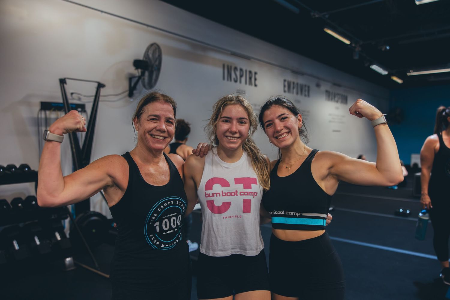 Three fitness enthusiasts showing off their arm muscles and smiling at the gym.