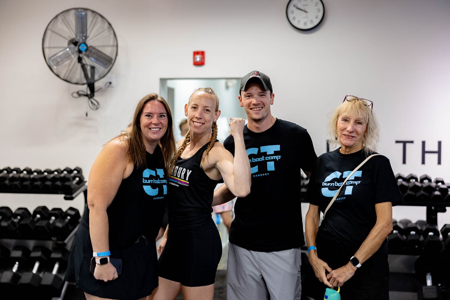 Exercise group poses together at a gym wearing matching black workout attire with light blue accents.