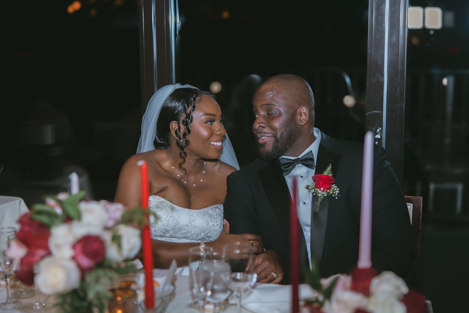 A couple shares an intimate moment at an elegant wedding reception with red and white table decorations.