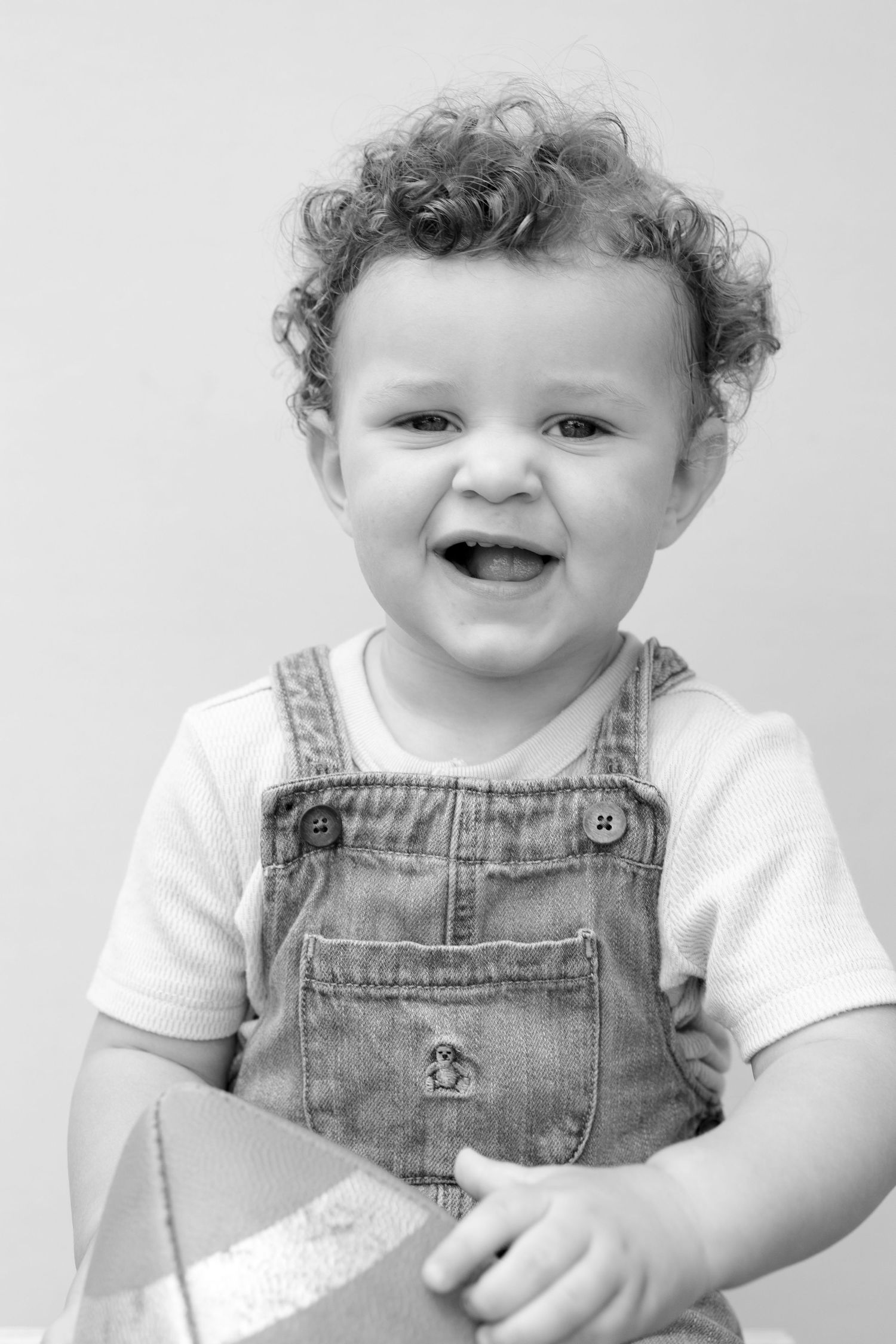 Black and white photo sequence of a toddler in denim overalls and white shirt showing joyful expressions.