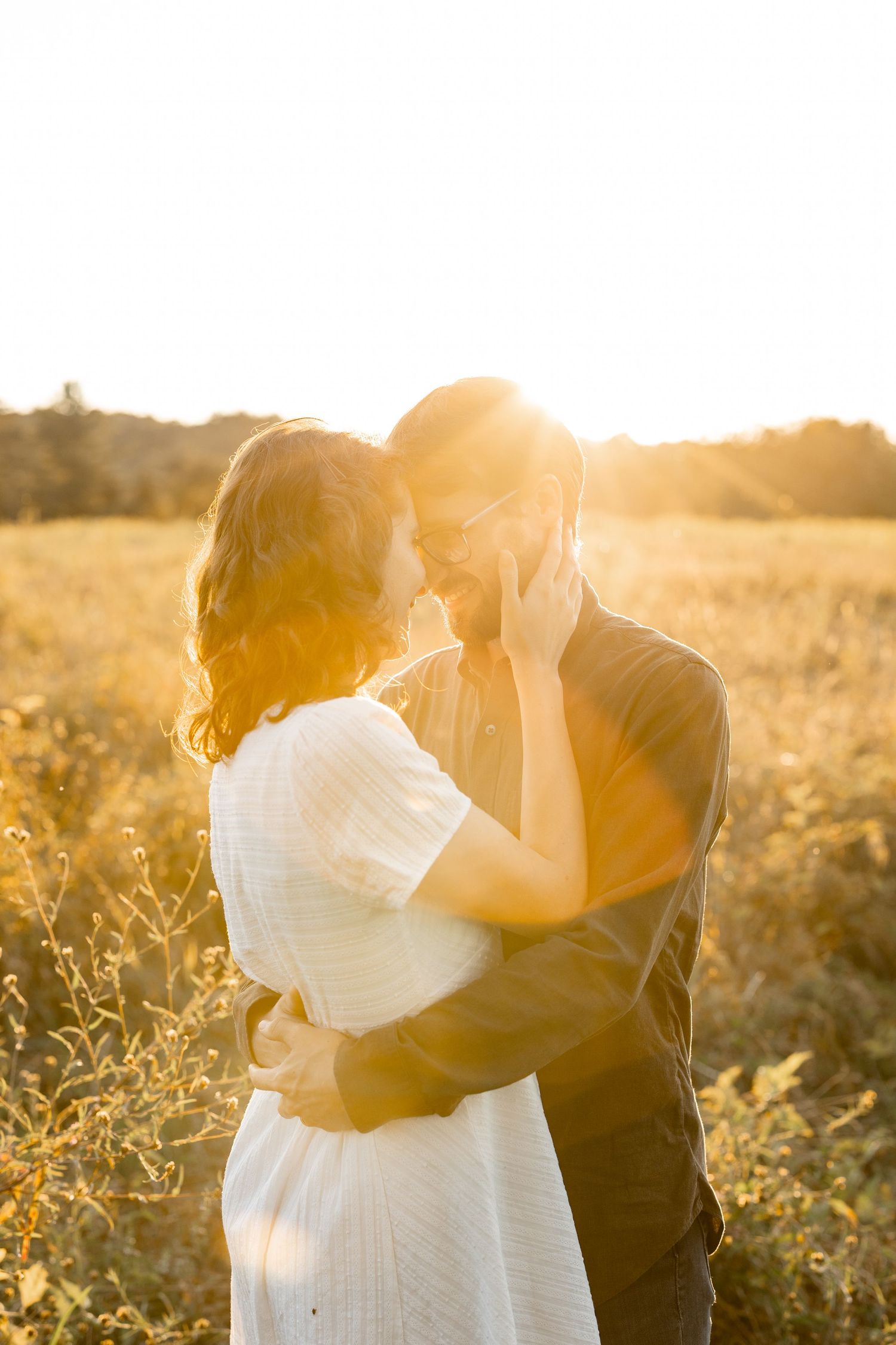 A couple shares an intimate moment in a sunlit meadow during golden hour.