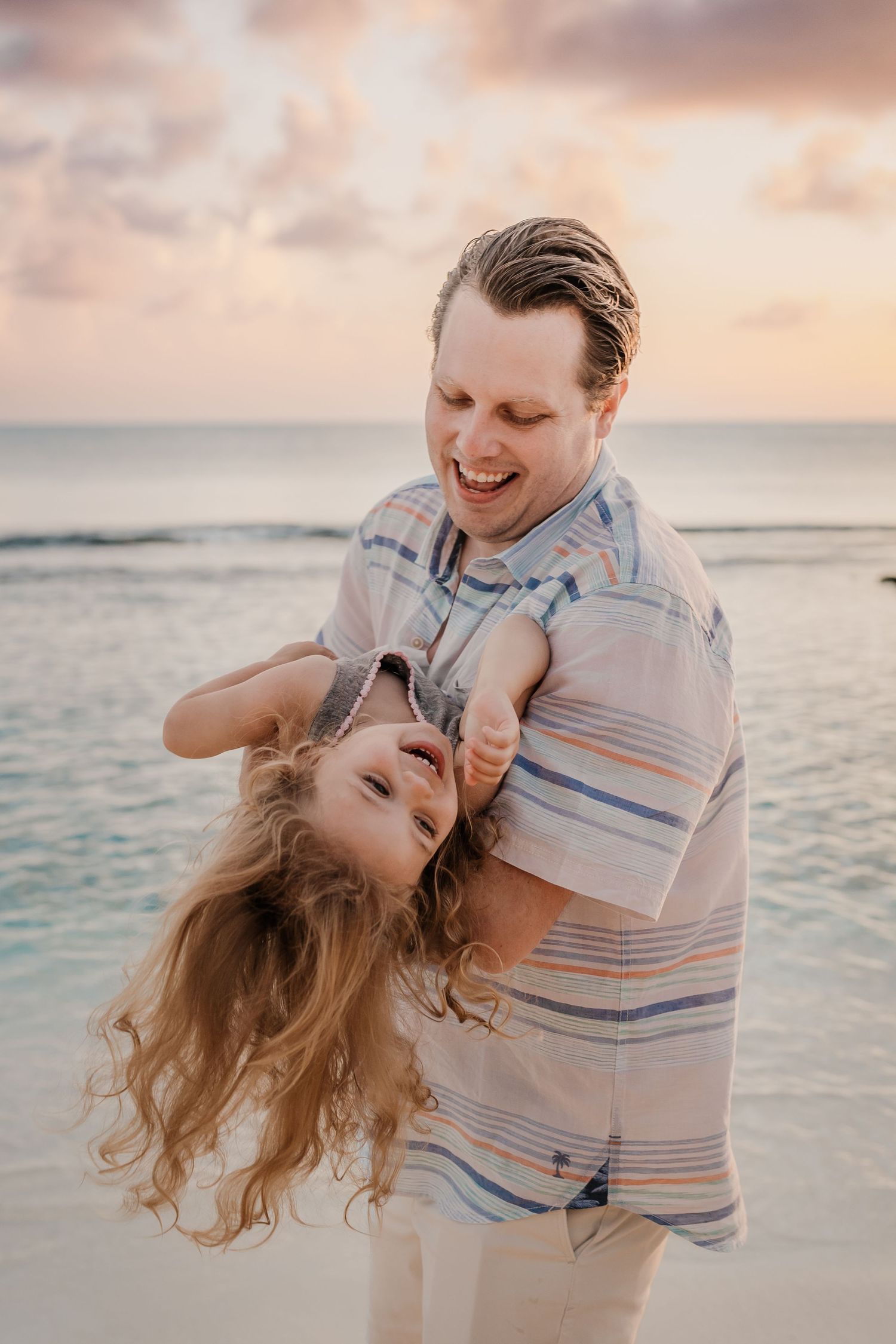 Playful beach portraits with couples laughing and embracing by the ocean at sunset.