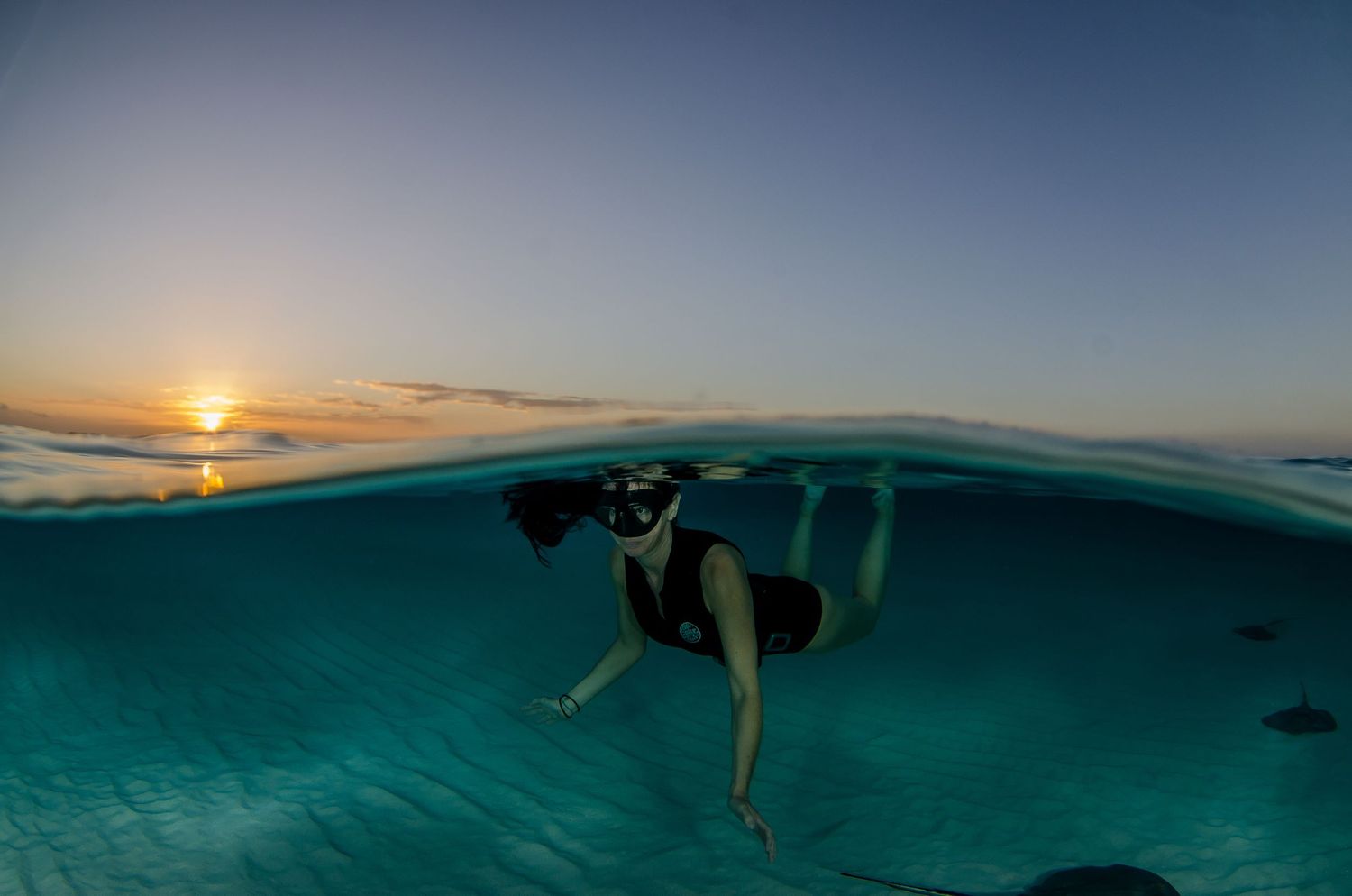 Split underwater view of ocean horizon during golden sunset with snorkeler silhouette.