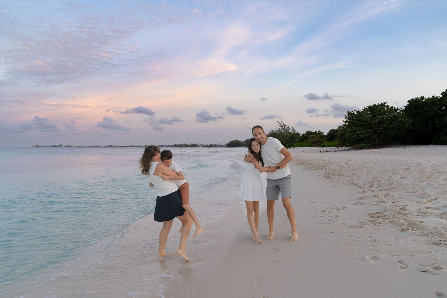 Two couples enjoying playful moments on a beach at dusk.