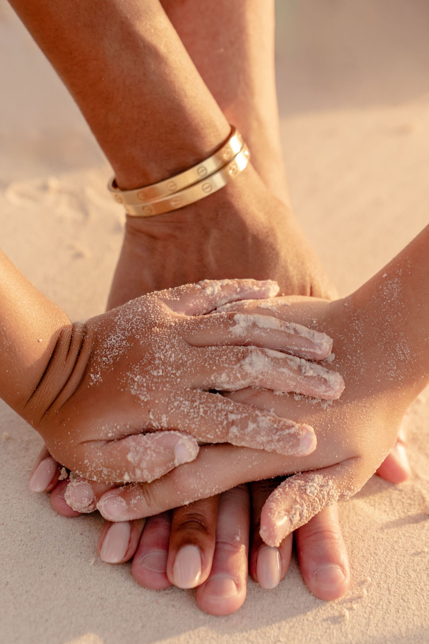 Close up of hands covered in sand touching each other on a sandy beach.