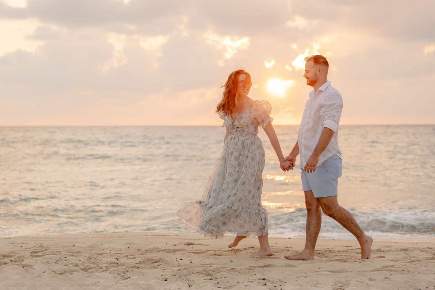 A couple walks hand in hand along the beach during golden hour.