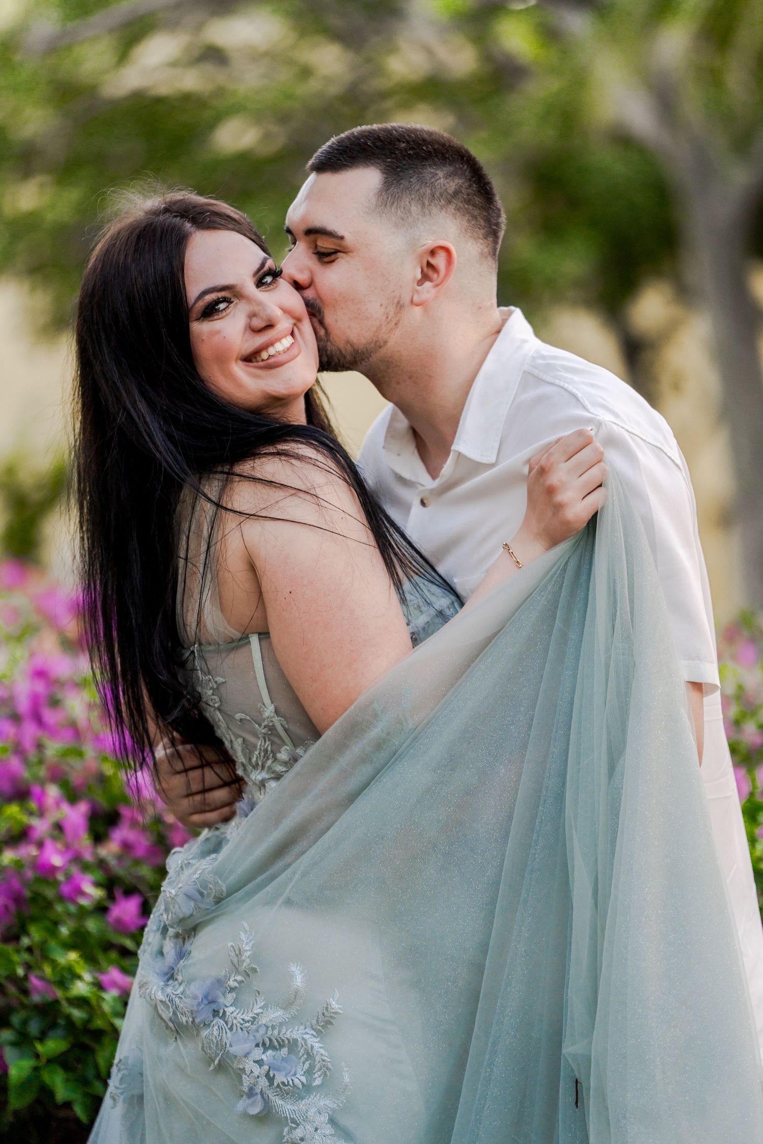 Romantic couple in white and blue embracing near pink flowers.