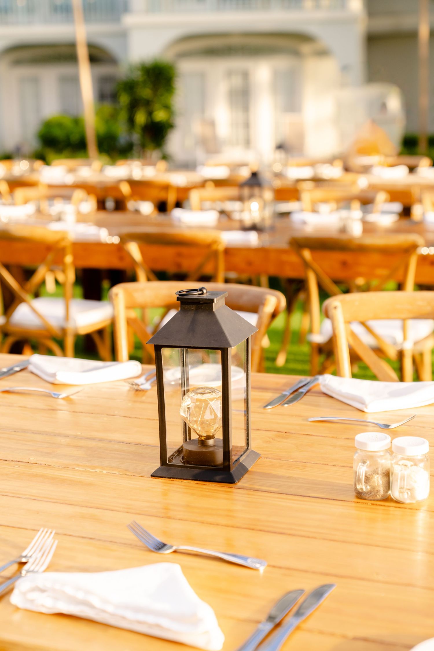 Elegant outdoor dining setup with wooden tables, lanterns and place settings.