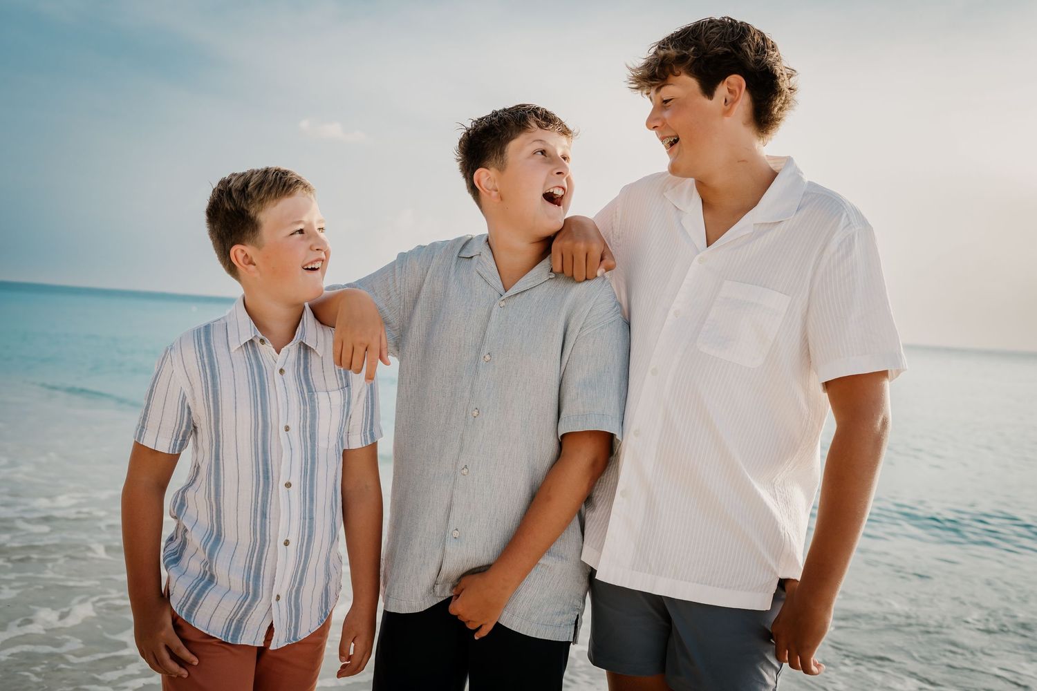 People in casual attire share laughs together against an ocean backdrop.