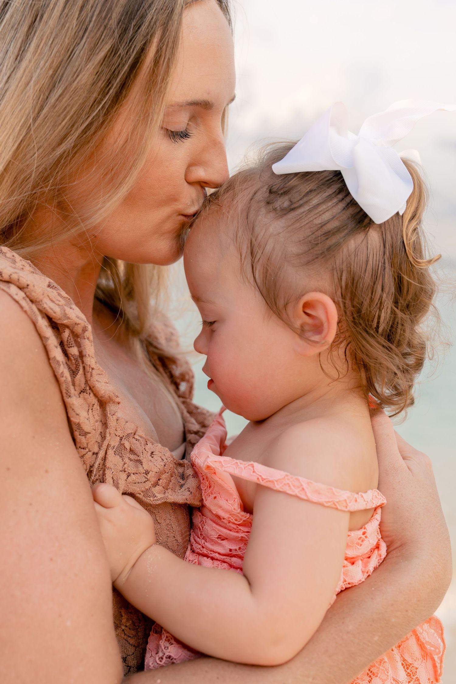 Intimate close-up moment between two people with a white bow accessory against an ocean backdrop.