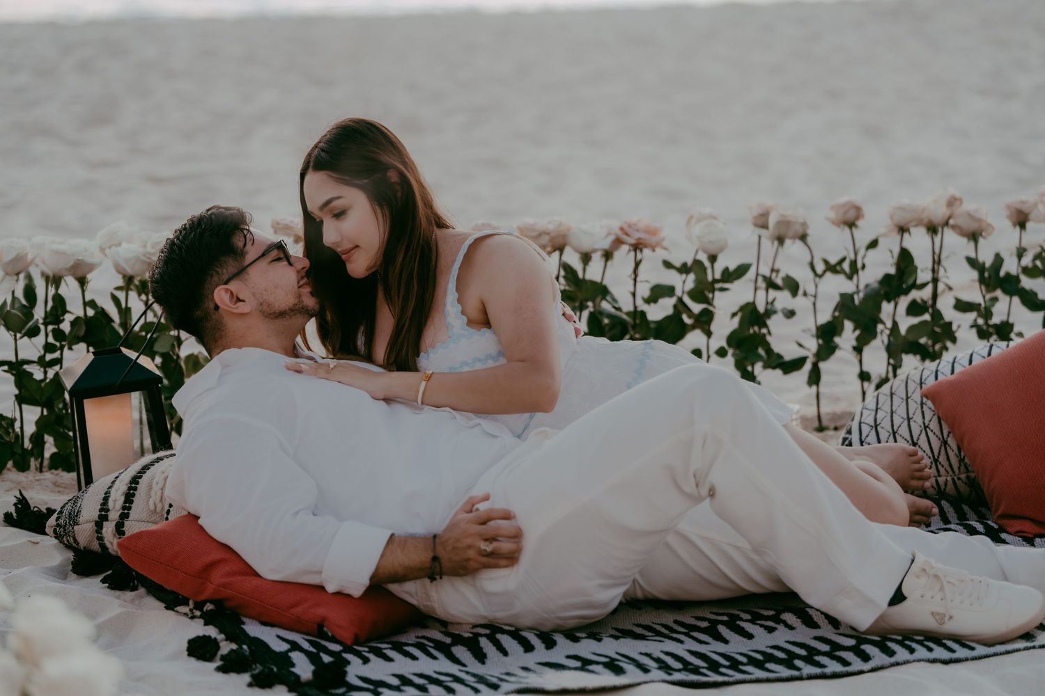 Couple sharing tender moment on beach blanket at sunset.
