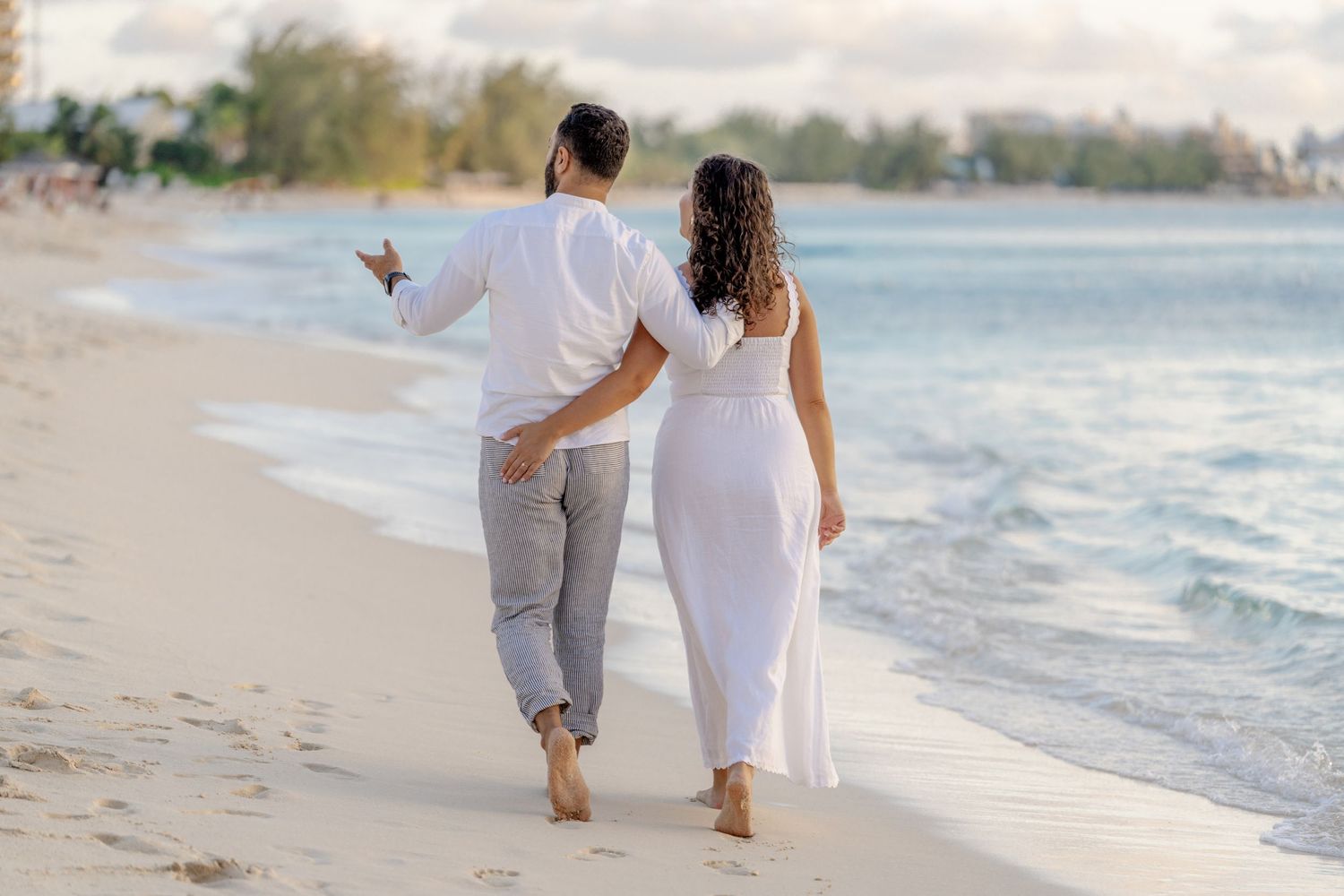 Couple walking hand in hand along a serene beach at sunset.