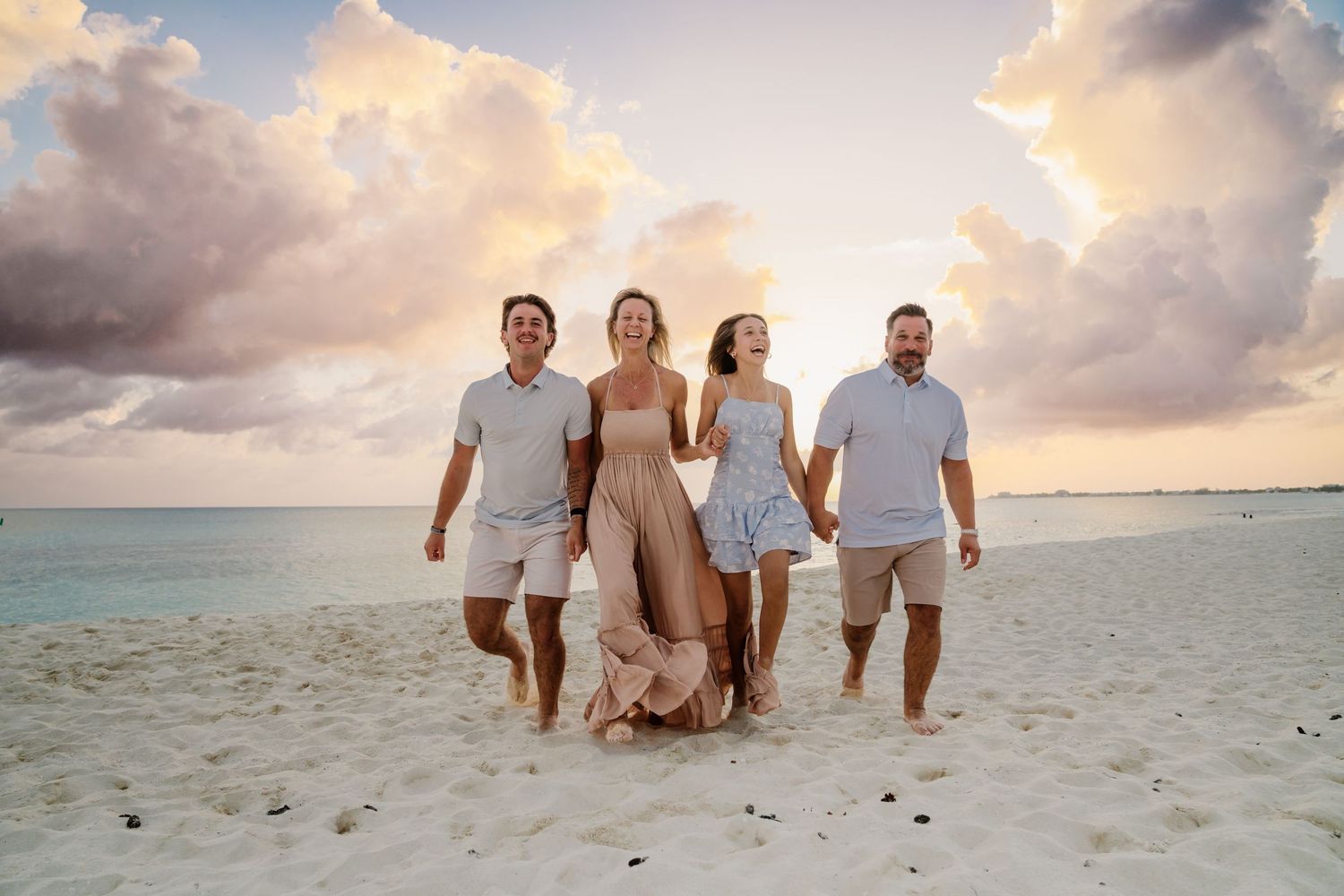 Family group runs together on sandy beach during dramatic sunset with clouds.