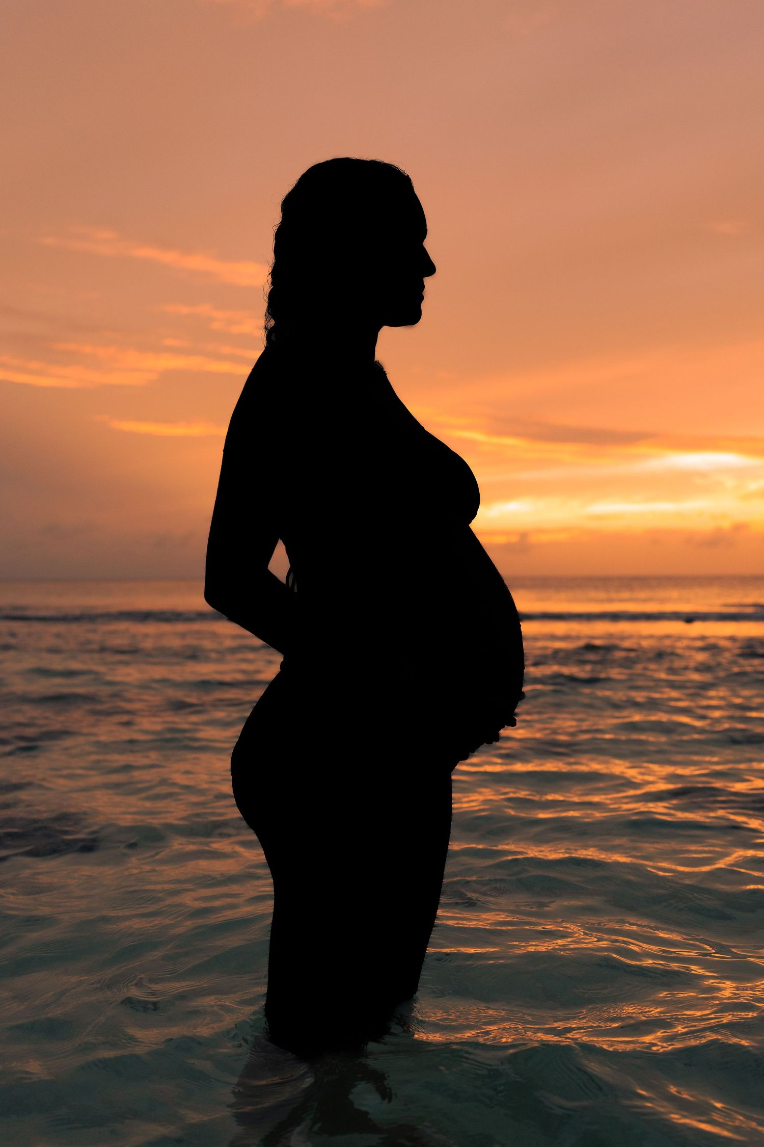 Silhouette portraits at sunset showing pregnant figure against dramatic ocean backdrop.