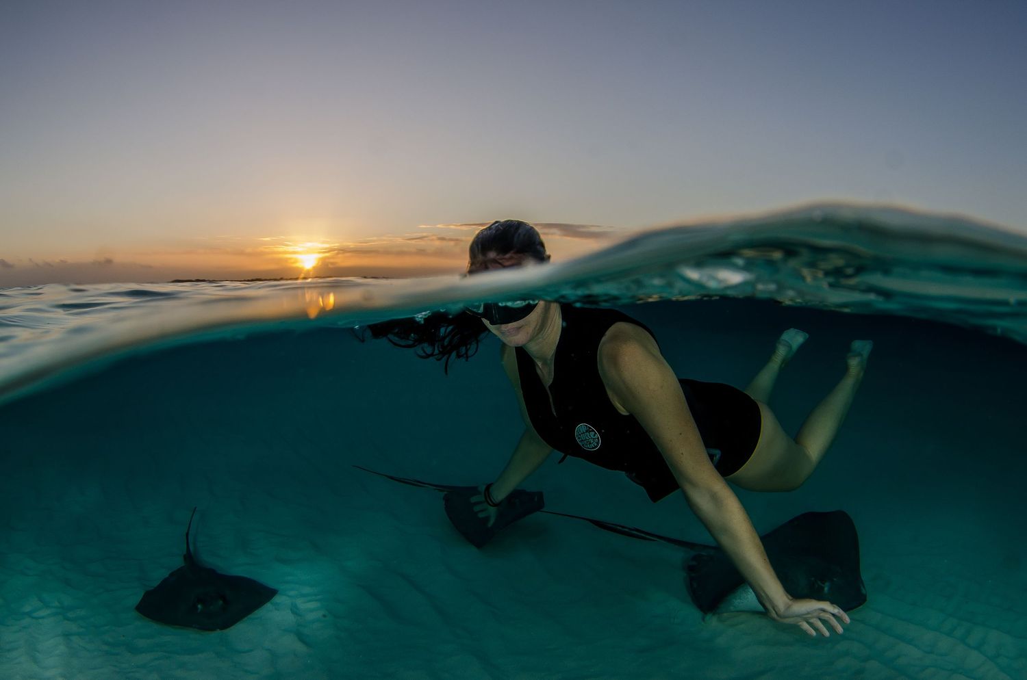 Split-shot photo captures sunset sky and underwater snorkeler in tropical ocean.