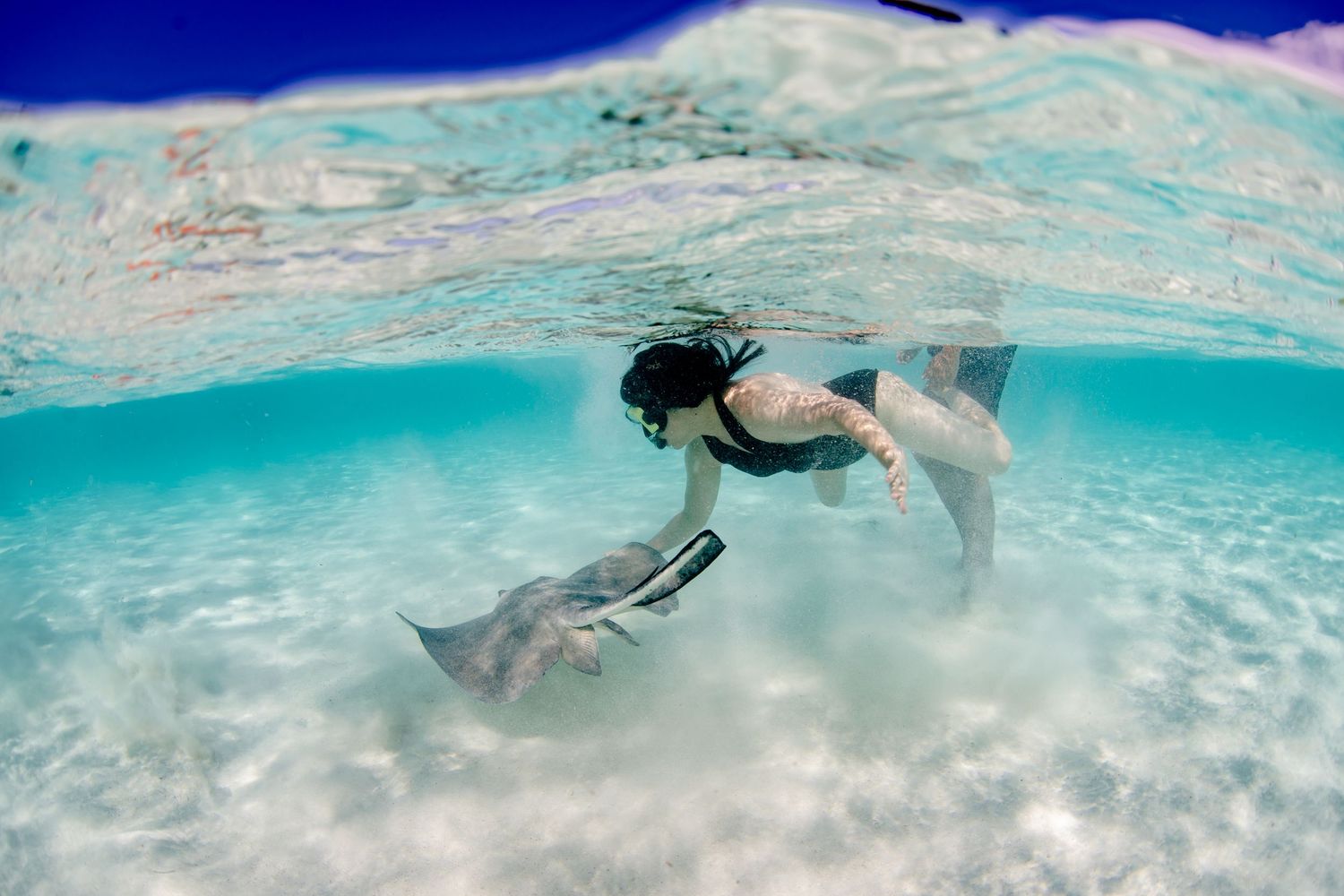 Underwater photography showing swimmers exploring crystal clear turquoise waters near a sandy ocean floor.
