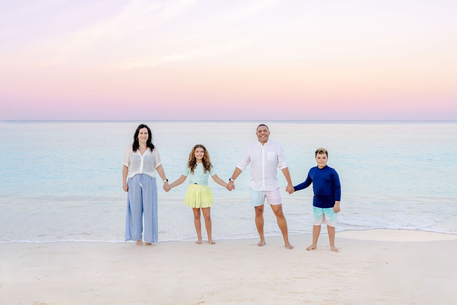 Family members walking hand in hand along a peaceful beach during golden hour.
