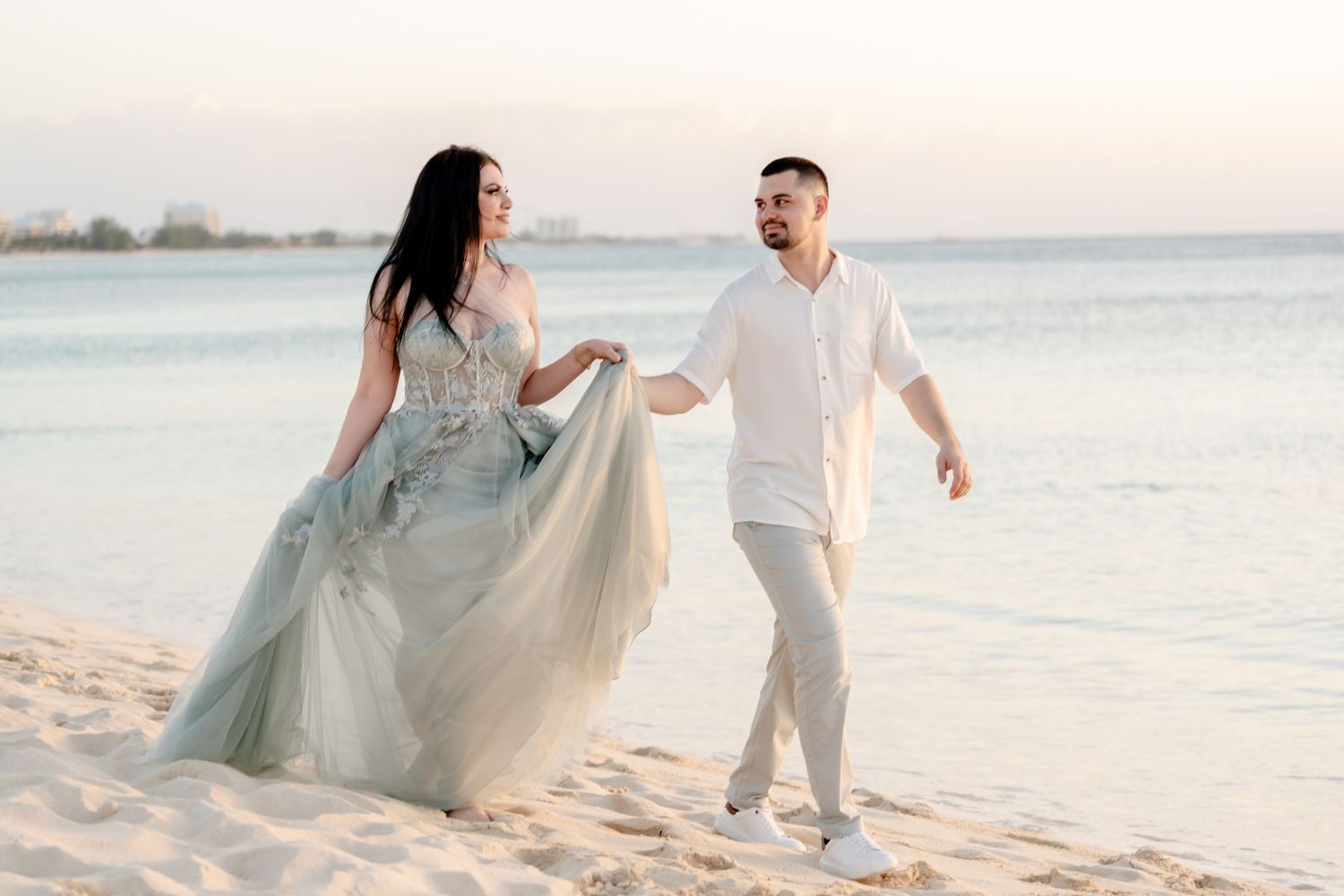 Couple in casual attire dances together on a sandy beach during golden hour.