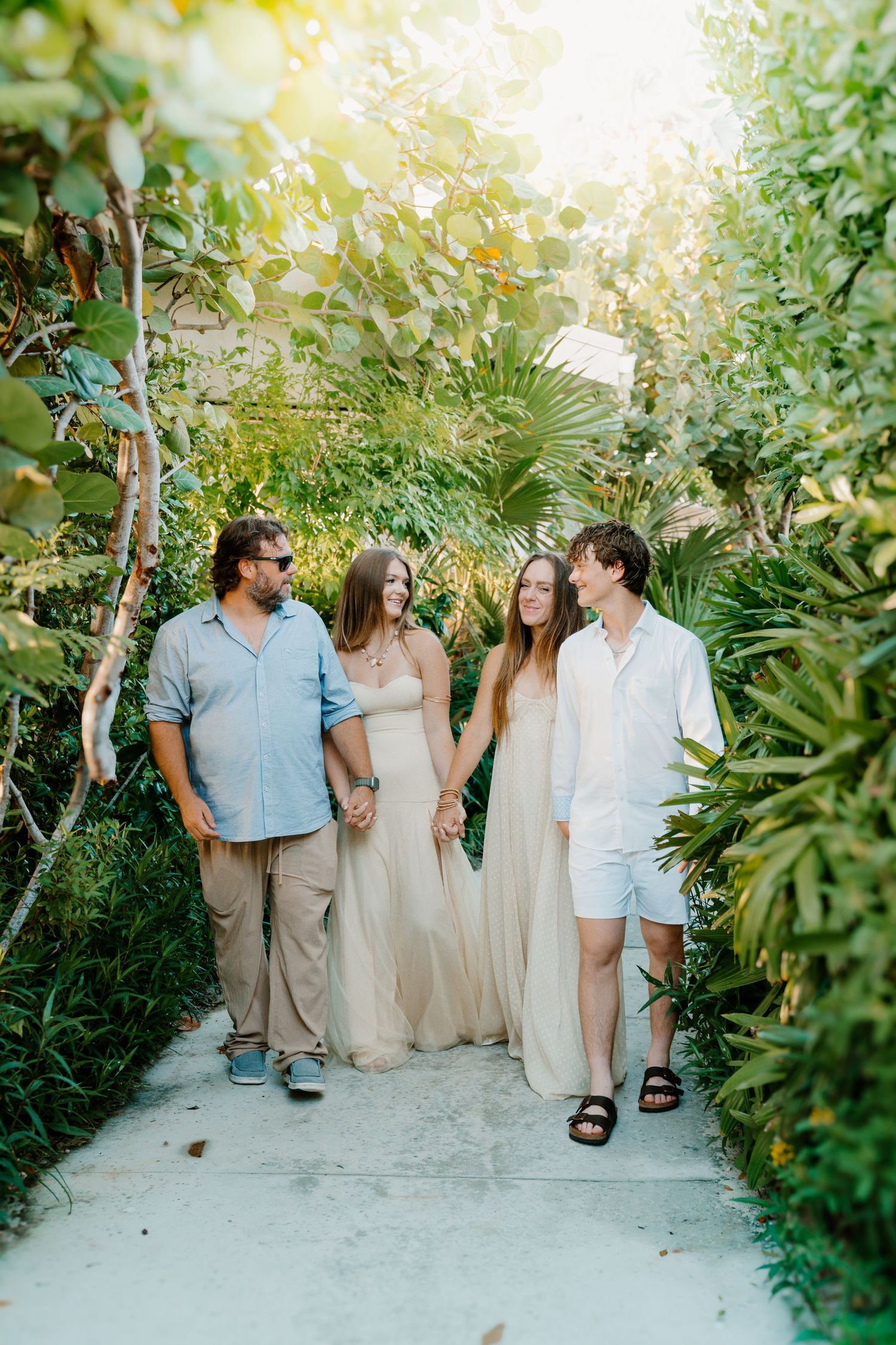 A group in light colored clothing walking along a lush garden path surrounded by tropical plants.