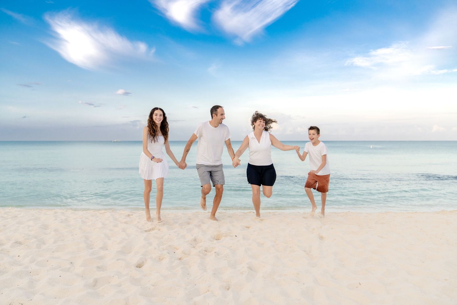 Group of people walking together on a pristine white sand beach with turquoise waters and wispy clouds overhead.