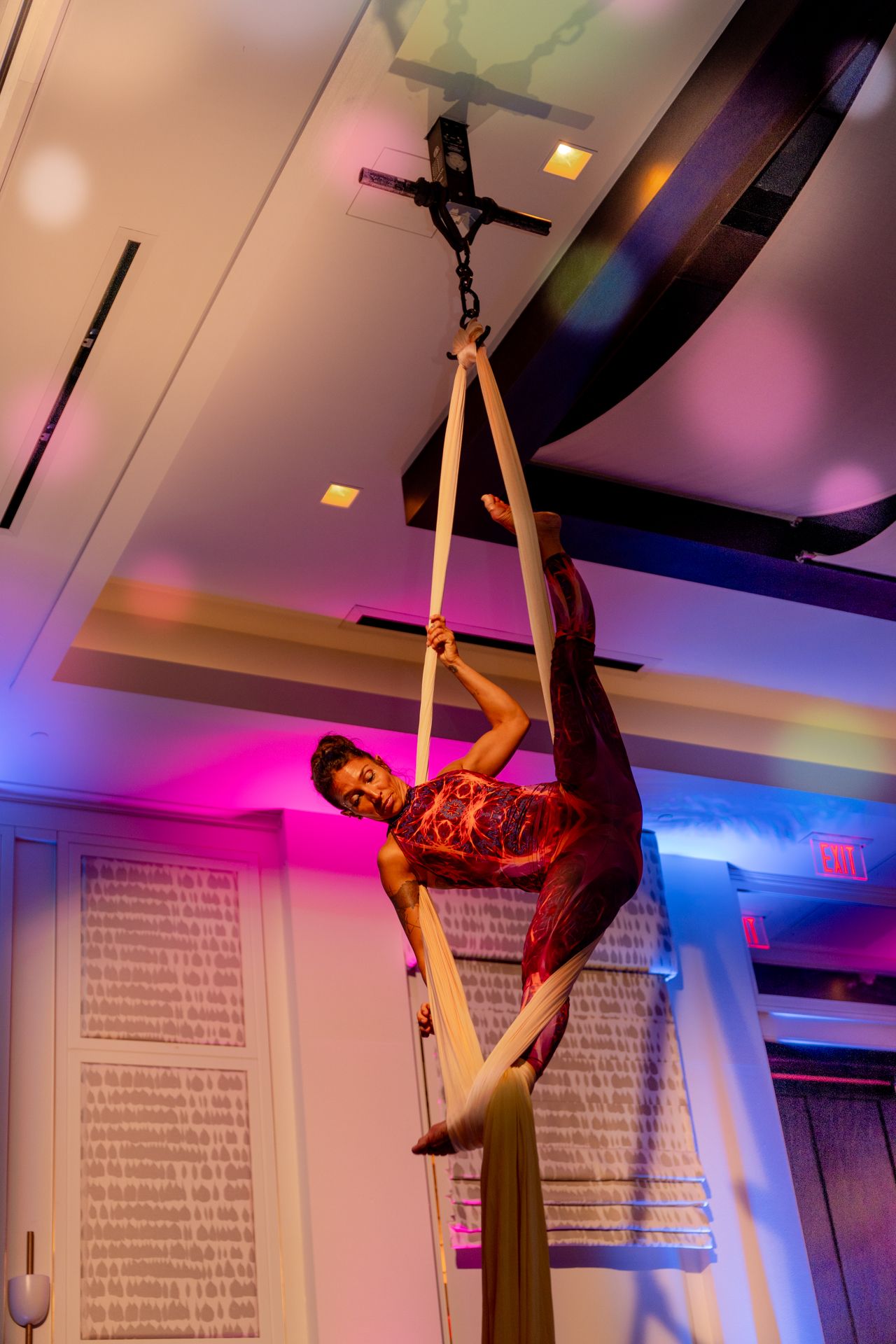 Aerial performer on silk ribbons illuminated by dramatic pink and purple stage lighting.
