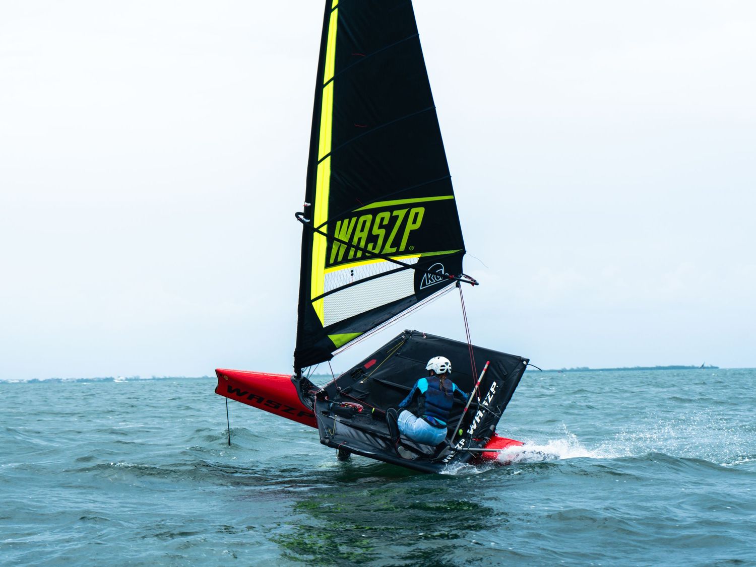 WASP sailing dinghy capsizing in choppy ocean water with yellow and black sail visible.