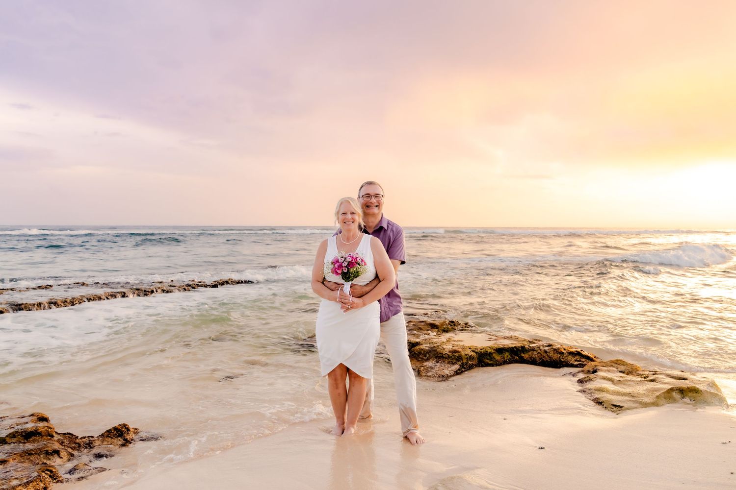 Couple walking together on a tropical beach at sunset with waves crashing on the shore.