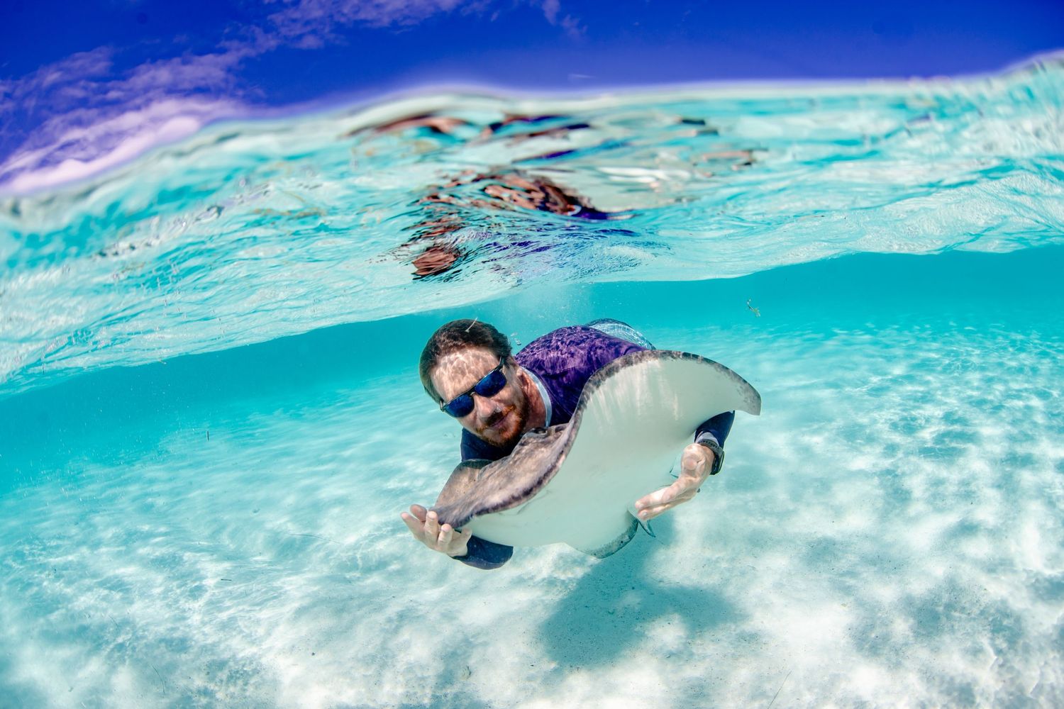 Swimmers glide through crystal clear turquoise waters over white sandy ocean floor.