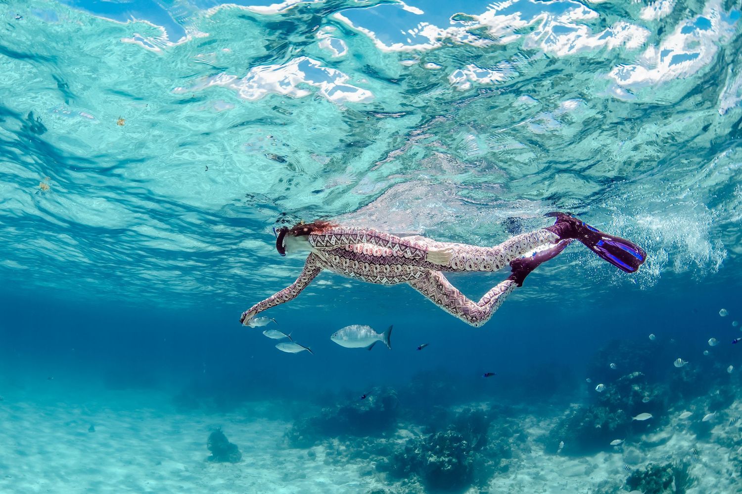 Snorkeler swimming through crystal clear tropical waters with fins.