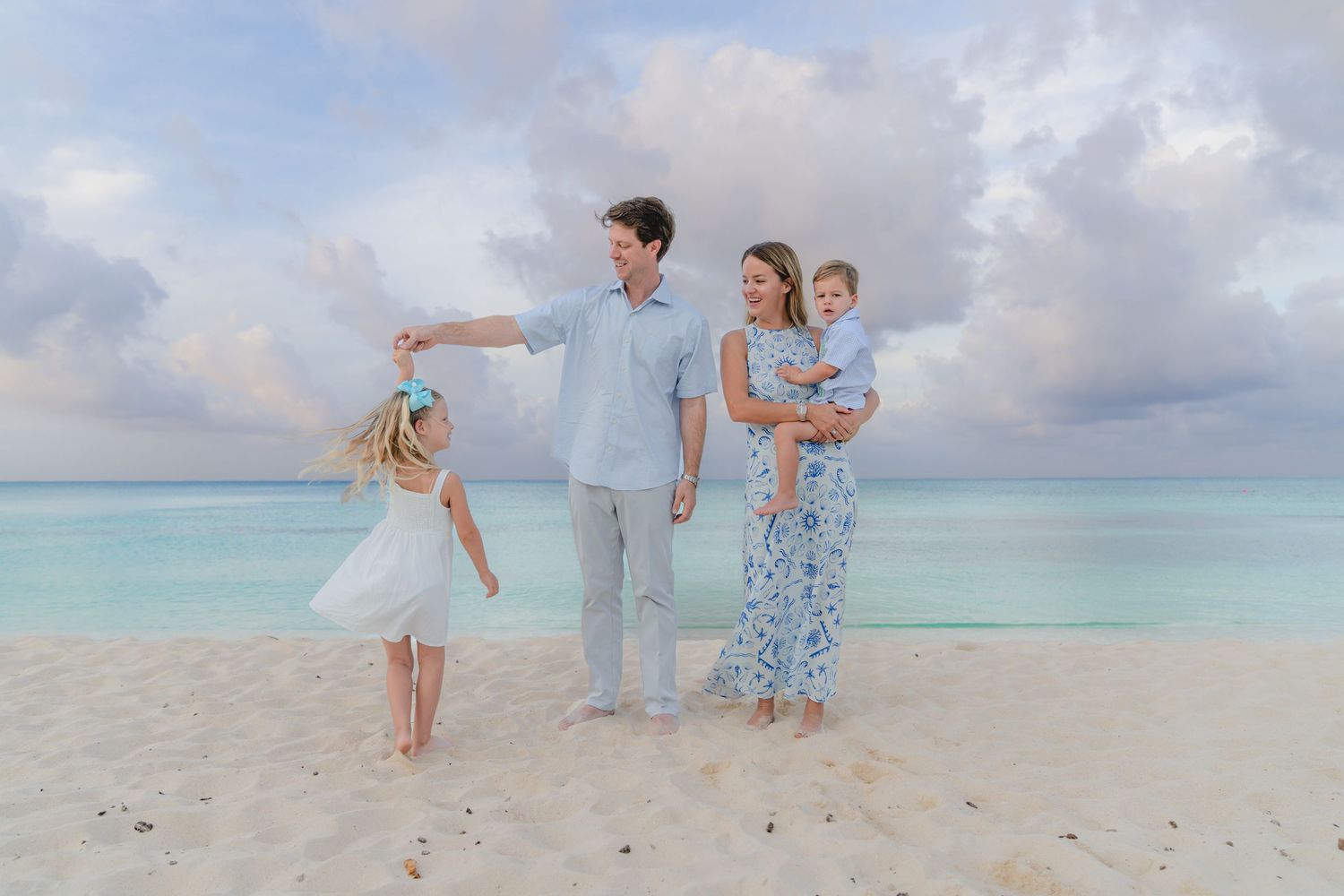 Family in coordinated blue and white outfits poses together on a pristine tropical beach at sunset.
