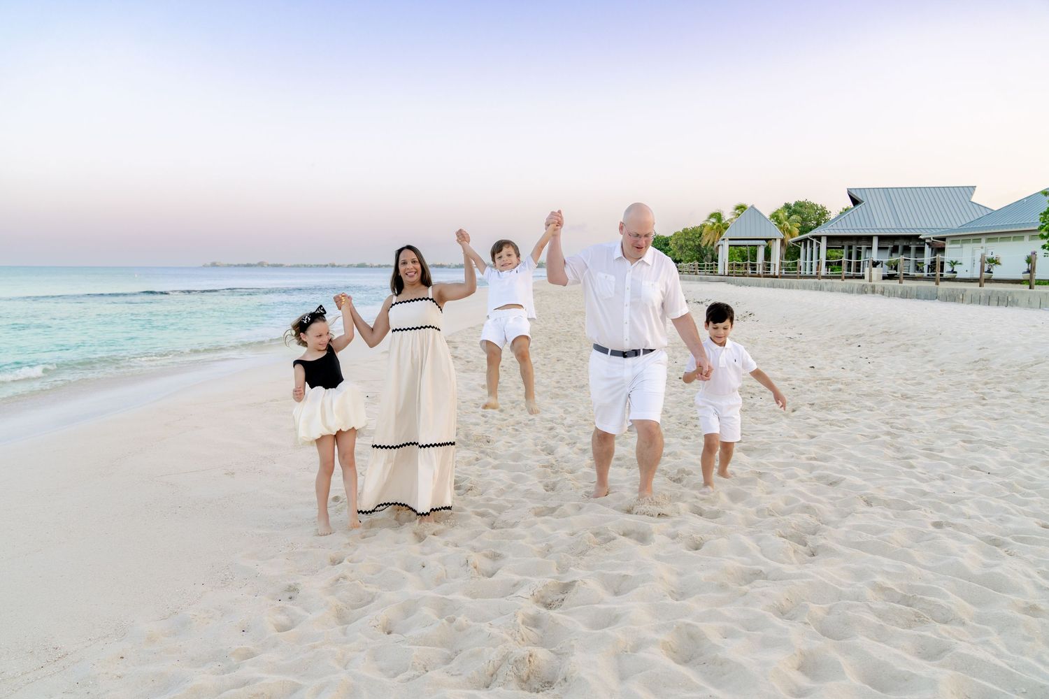 Group in white outfits jumping and playing on beach with resort buildings in background.