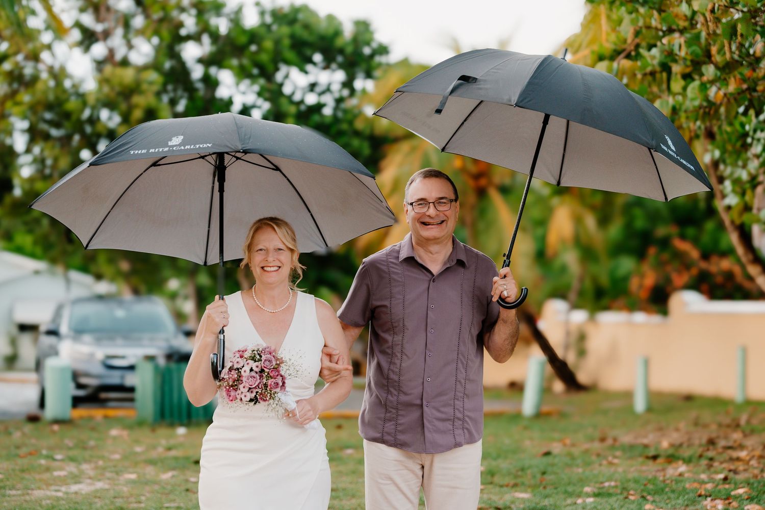 Couple posing with umbrellas in a lush green garden setting.