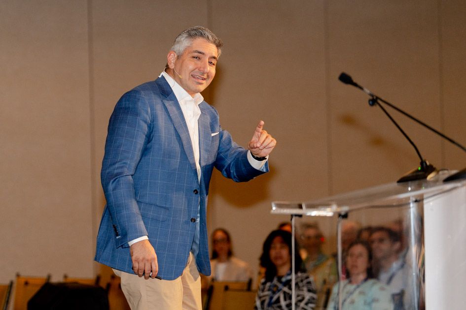 Speaker in a blue blazer presenting on stage at a corporate event.